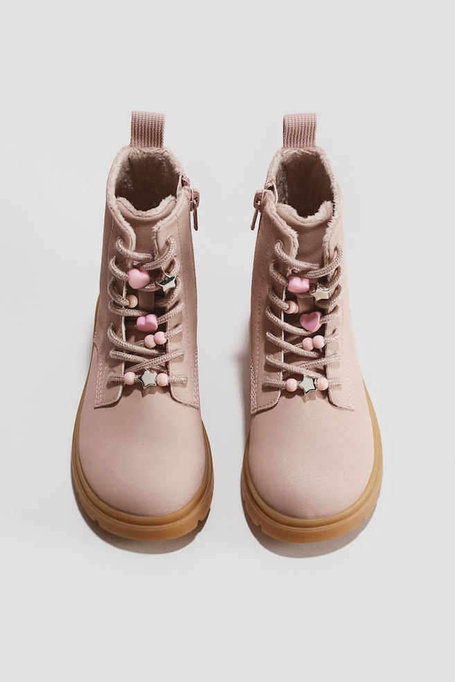 A pair of pink high-top lace-up boots is shown from a front-facing angle, featuring gum-coloured lug soles and inner side zips. The matching pink laces are decorated with pink heart and round beads, alongside silver star charms, with a soft faux-fur lining visible at the collar. - 1