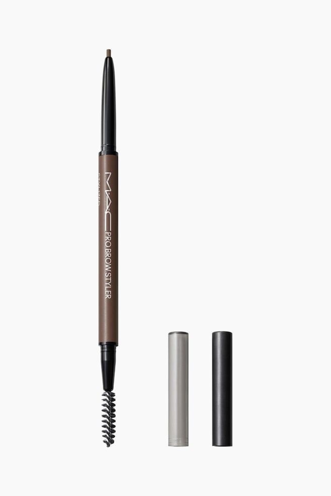 Pro Brow Styler Ã¸yenbrynsblyant med to ender stÃ¥r vertikalt, og viser en fin, uttrekkbar brun spiss Ã¸verst og en svart spoolie-bÃ¸rste nederst. Ved siden av blyanten stÃ¥r to separate hetter â Ã©n sÃ¸lvfarget og Ã©n svart â oppreist. - 1
