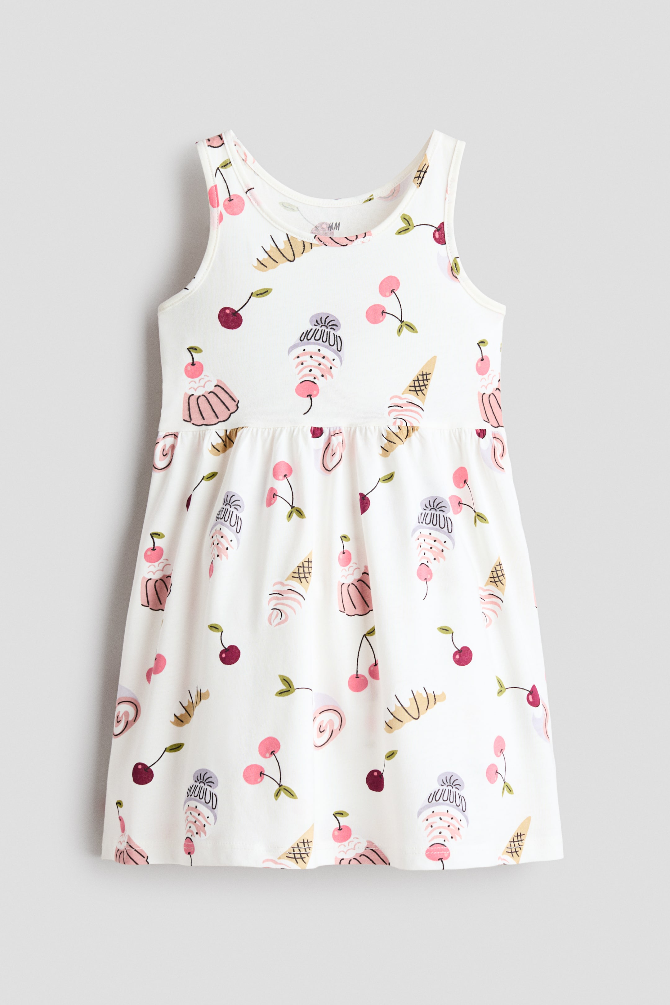 View larger image: A white sleeveless dress featuring a rounded neckline and an all-over print of cherries, ice cream cones, sundaes, and cupcakes. The dress gathers at the waist, creating a flared skirt.
