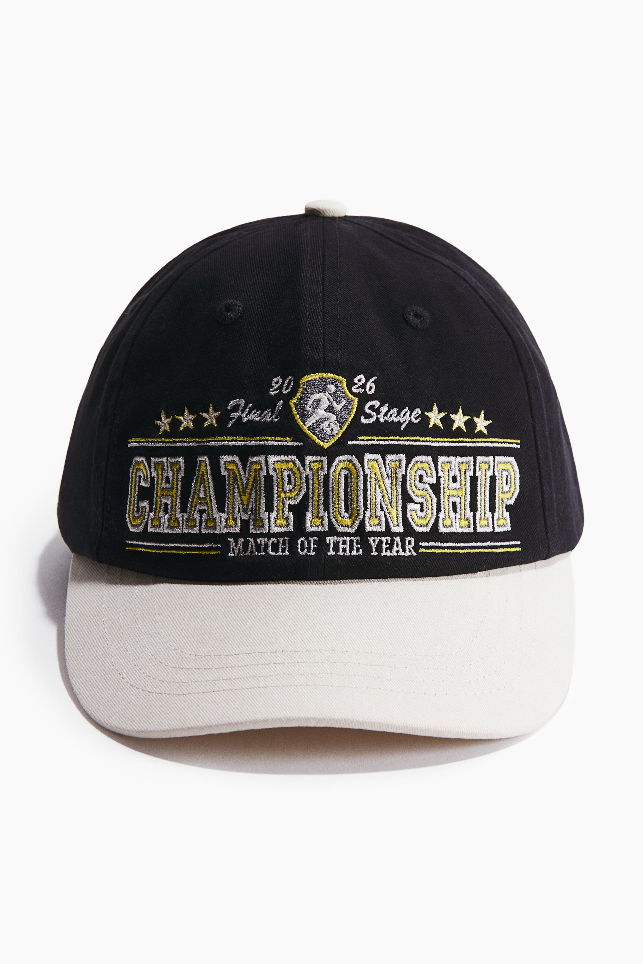 View larger image: The baseball cap showcases a black crown paired with an off-white brim. The crown is adorned with gold and white embroidered text that reads 'CHAMPIONSHIP' alongside '20 FINAL 26 STAGE' and features a shield emblem with a running figure, with 'MATCH OF THE YEAR' embroidered beneath.