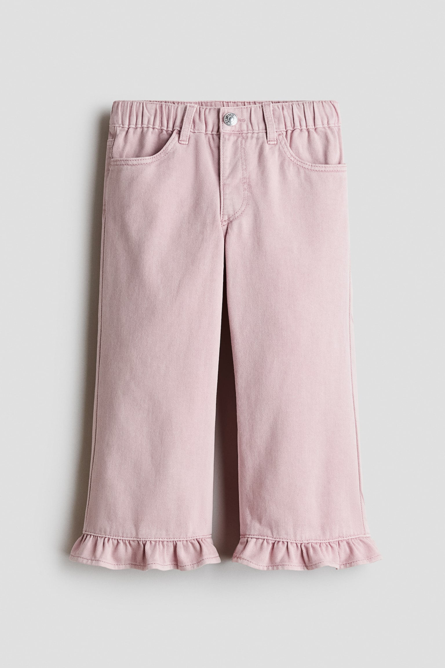 Un pantalon en denim rose clair est prÃ©sentÃ© de face, avec une taille Ã©lastiquÃ©e munie de passants pour ceinture, une fermeture Ã  bouton unique et des poches italiennes Ã  lâavant. Ce pantalon Ã  jambe droite met en valeur des dÃ©tails Ã  volants le long des ourlets infÃ©rieurs.