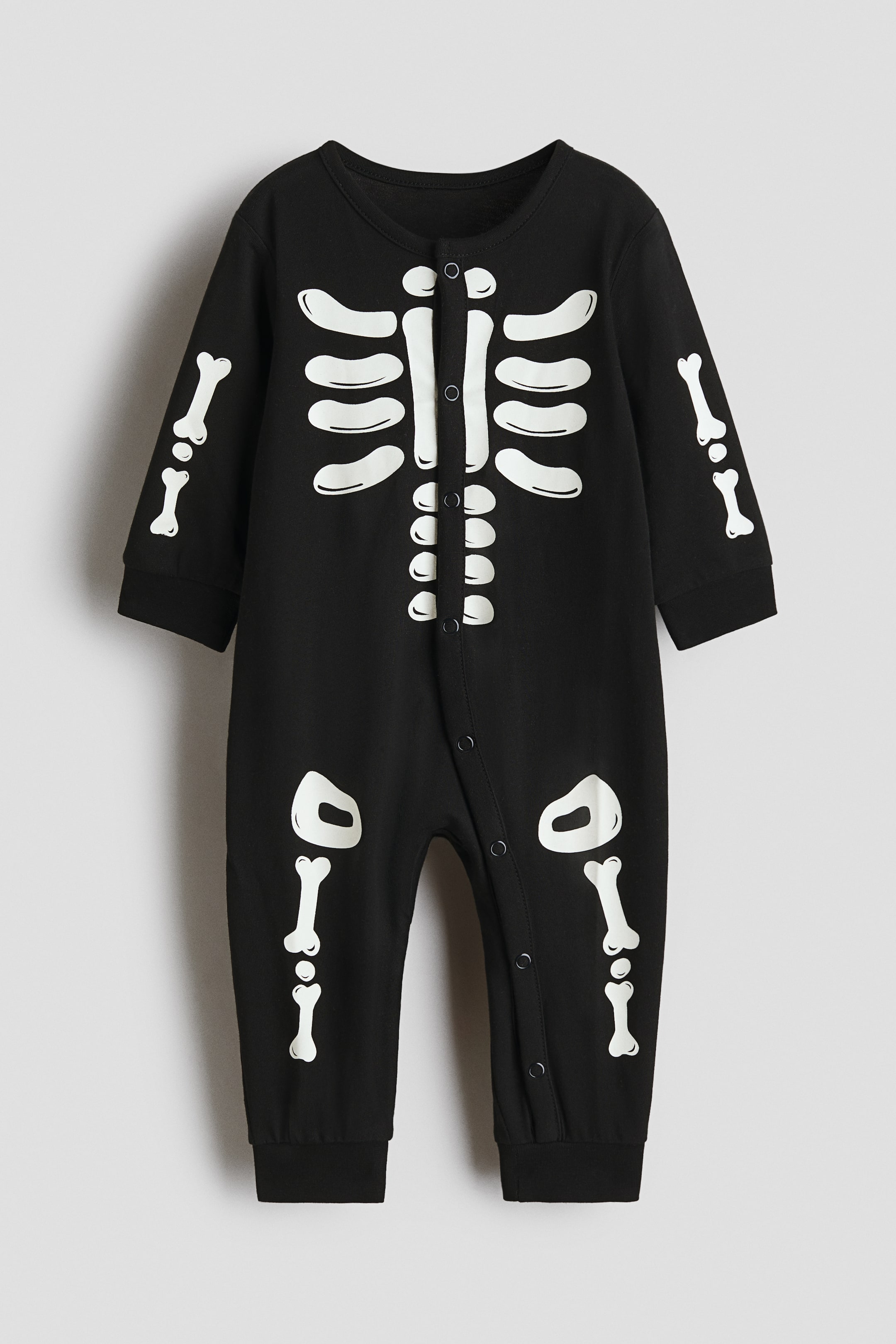 View larger image: A sleepsuit in super-soft cotton jersey is shown front-facing, featuring an all-over white skeleton print. It is designed with long sleeves with banded cuffs, long legs with banded hems, and white press-studs running down the centre front and along the inner left leg for easy changing.