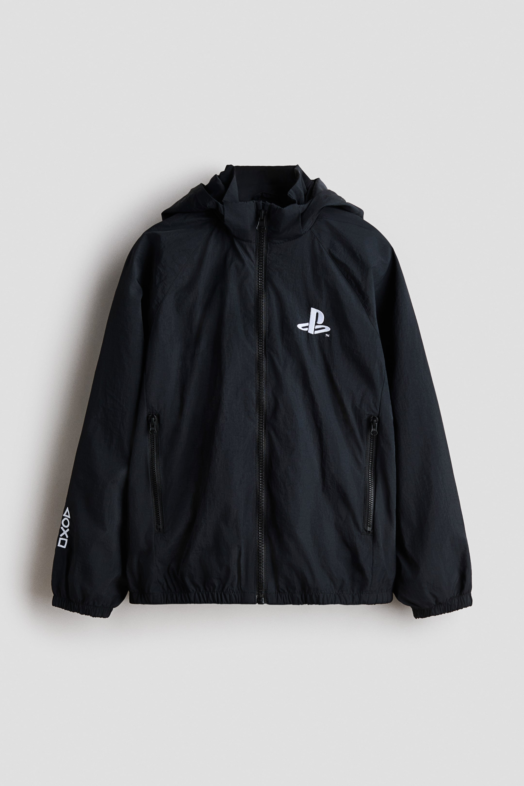View larger image: A black hooded jacket features a white PlayStation logo on the left chest. A full-length black zipper closes the front, and two black zippered pockets appear on the lower front. White PlayStation controller symbols are vertically arranged on the left sleeve cuff, and elasticized cuffs and hem complete the design.