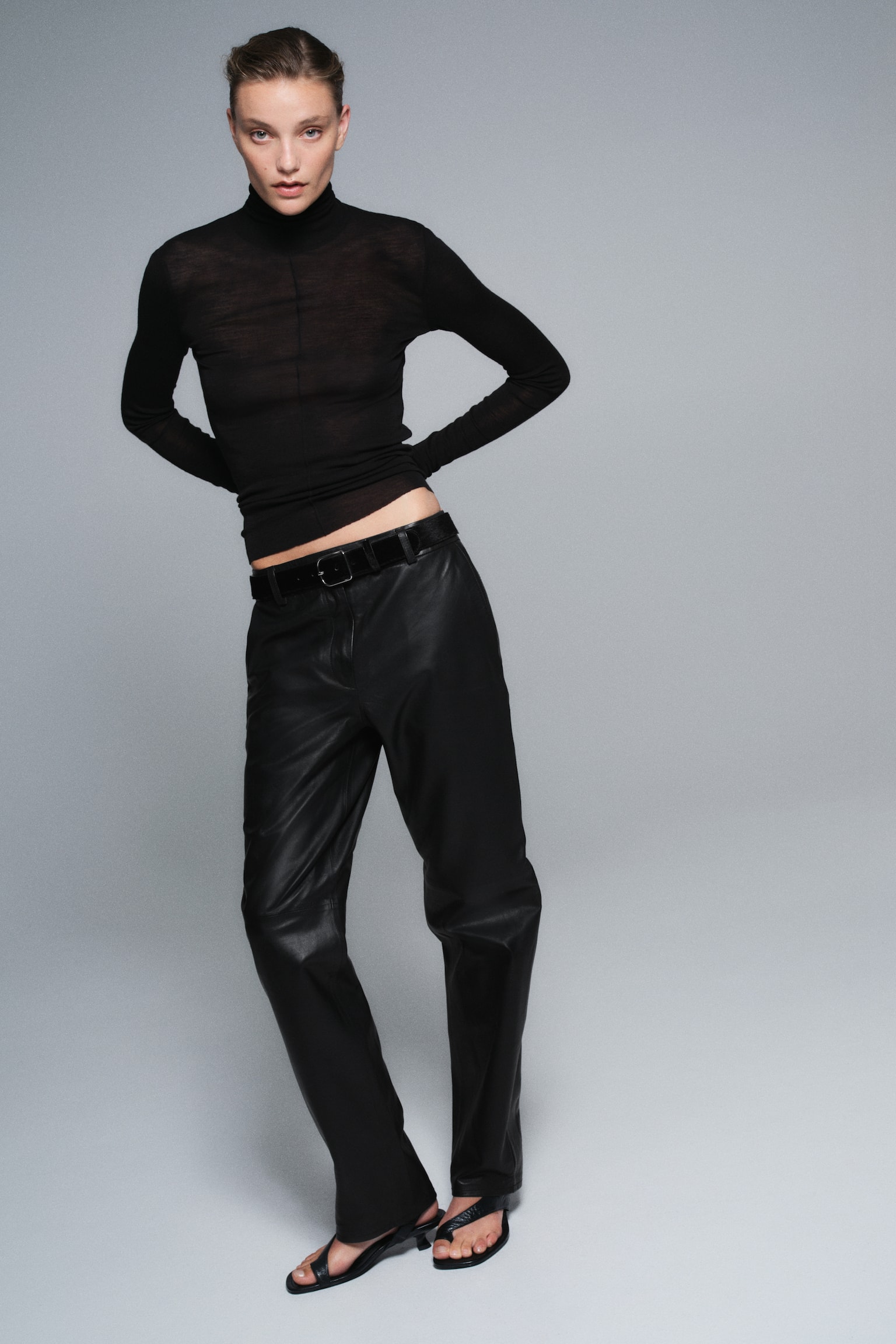 Black leather trousers, viewed from the front, feature a straight-leg silhouette with a structured waistband and belt loops. A horizontal seam runs across the mid-thigh area of each leg, highlighting the textured leather material. - 1