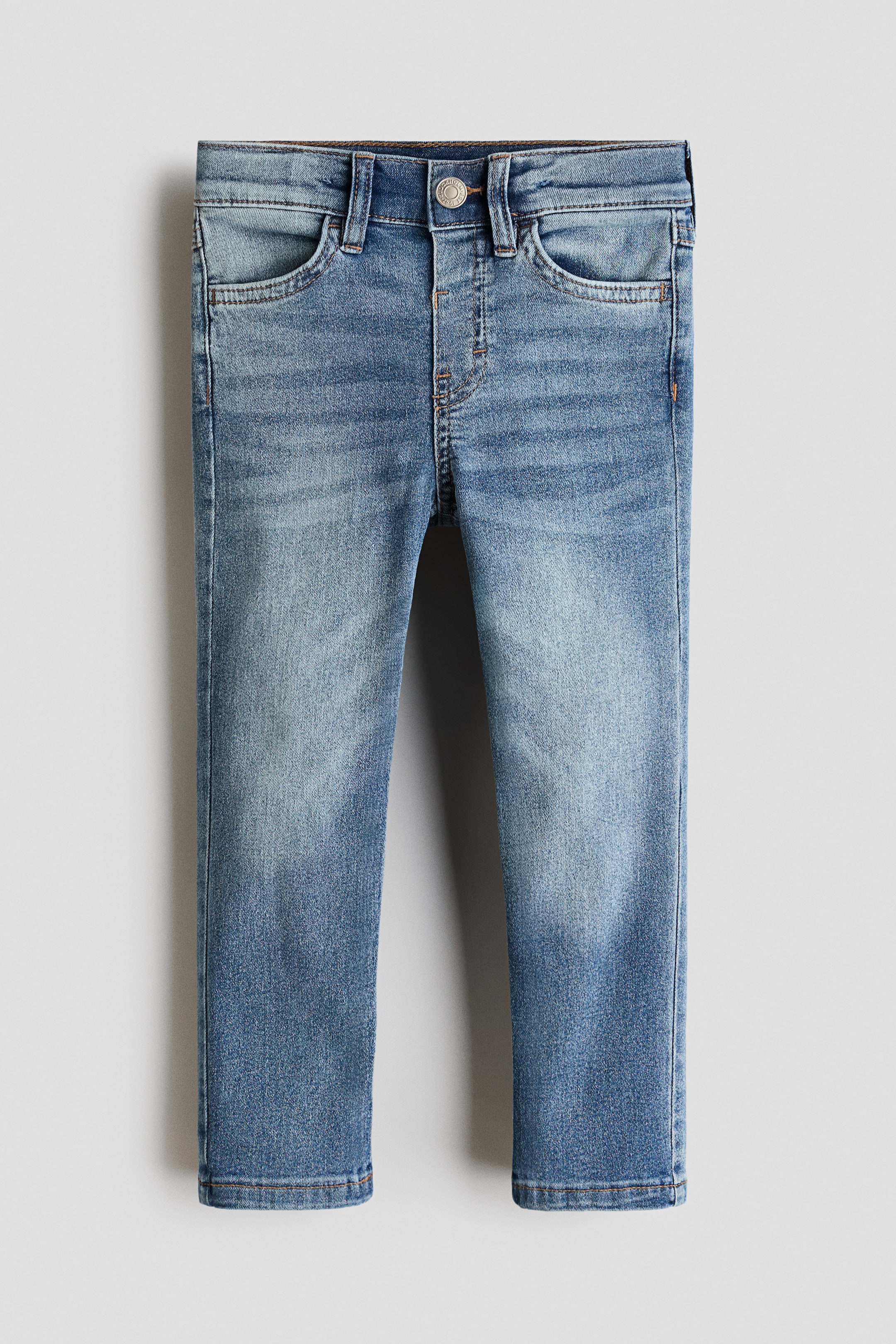 View larger image: Front-facing jeans showcase a slim fit in washed, medium blue stretch denim, featuring a flat waistband with belt loops, a single metal button, a faux fly, and two curved front pockets.