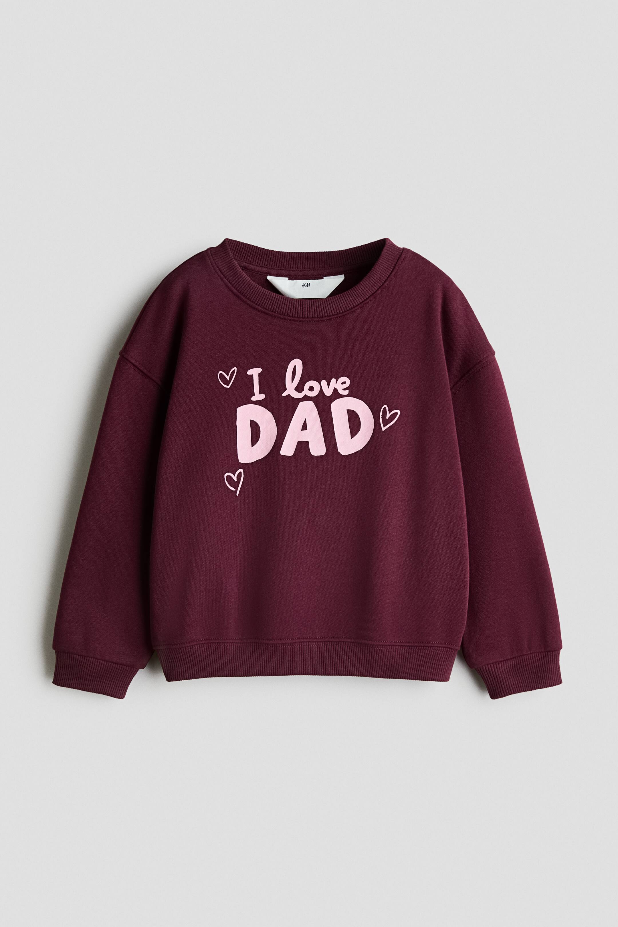 View larger image: A front-facing burgundy sweatshirt features a ribbed crew neck, drop shoulders, ribbed cuffs, and a ribbed hem. The chest displays the printed pink text "I love DAD" surrounded by three small hand-drawn hearts.
