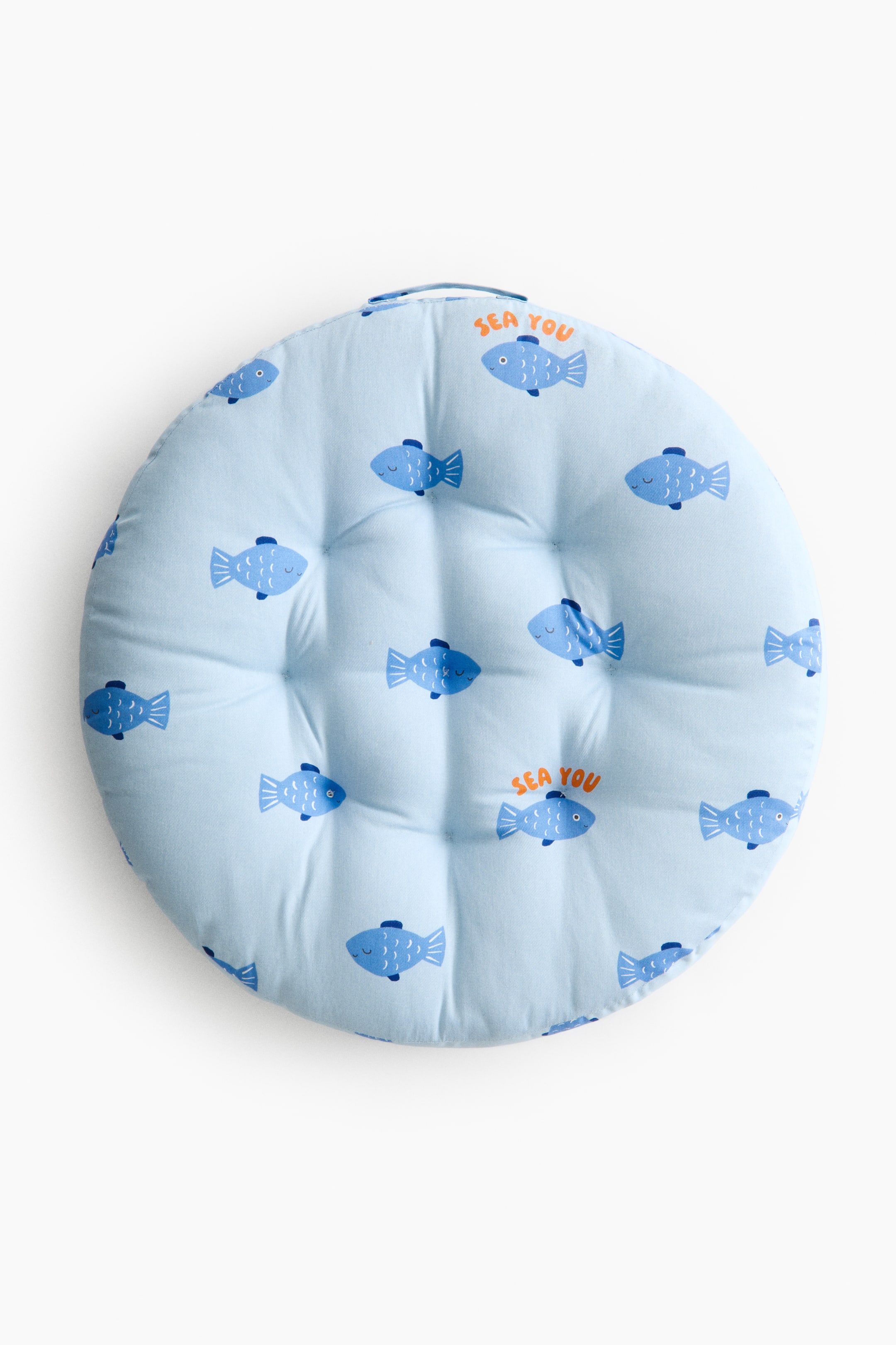 View larger image: A round cushion is presented front-facing, featuring a light blue fabric with a repeating pattern of blue fish, some accented with orange "SEA YOU" text. The cushion is tufted across its surface and includes a fabric loop handle at the top.