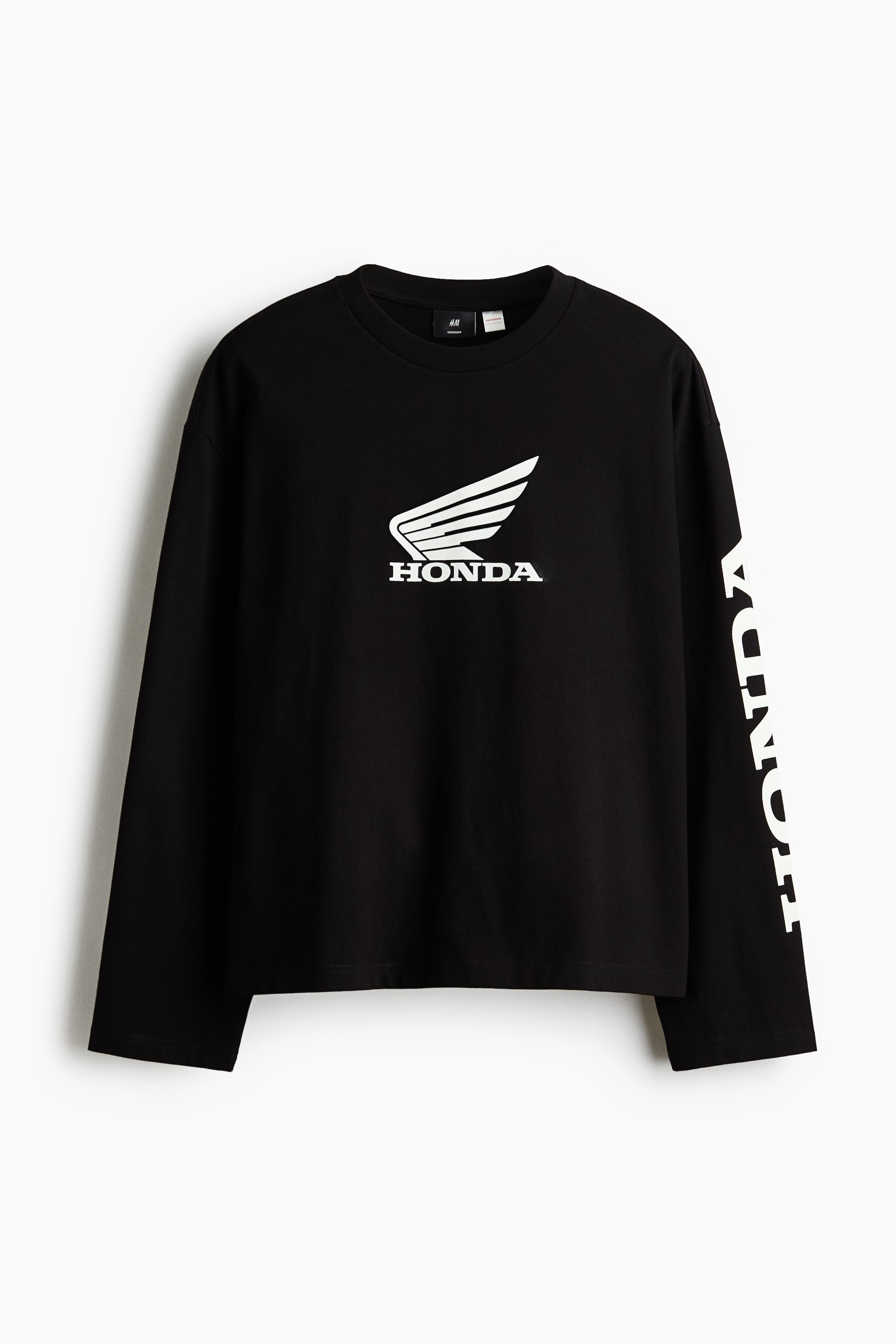 Visualizza immagine più grande: Una t-shirt nera a maniche lunghe mostra il davanti. Presenta il logo alato bianco di Honda sopra la scritta "HONDA" sul petto e la scritta "HONDA" stampata in verticale in bianco lungo il lato esterno di entrambe le maniche.