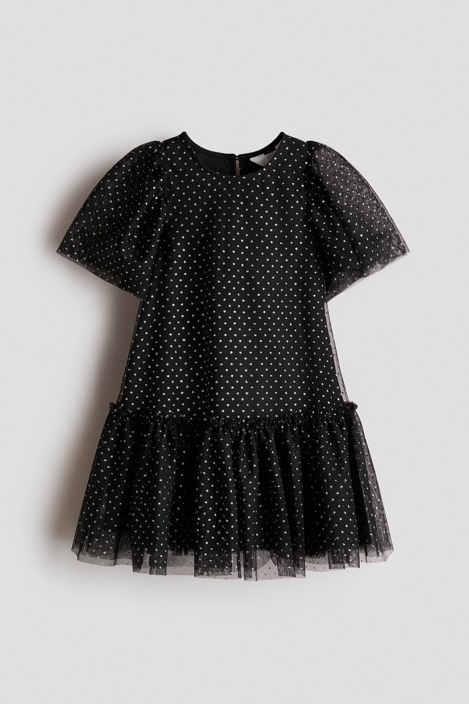 Ein schwarzes Kleid ist von vorne zu sehen, mit einem transparenten TÃ¼ll-Ãberwurf und einem allover Muster aus kleinen metallisch silbernen Punkten. Das Kleid zeigt kurze PuffÃ¤rmel, einen runden Ausschnitt und einen gerafften, gerÃ¼schten Saum.
