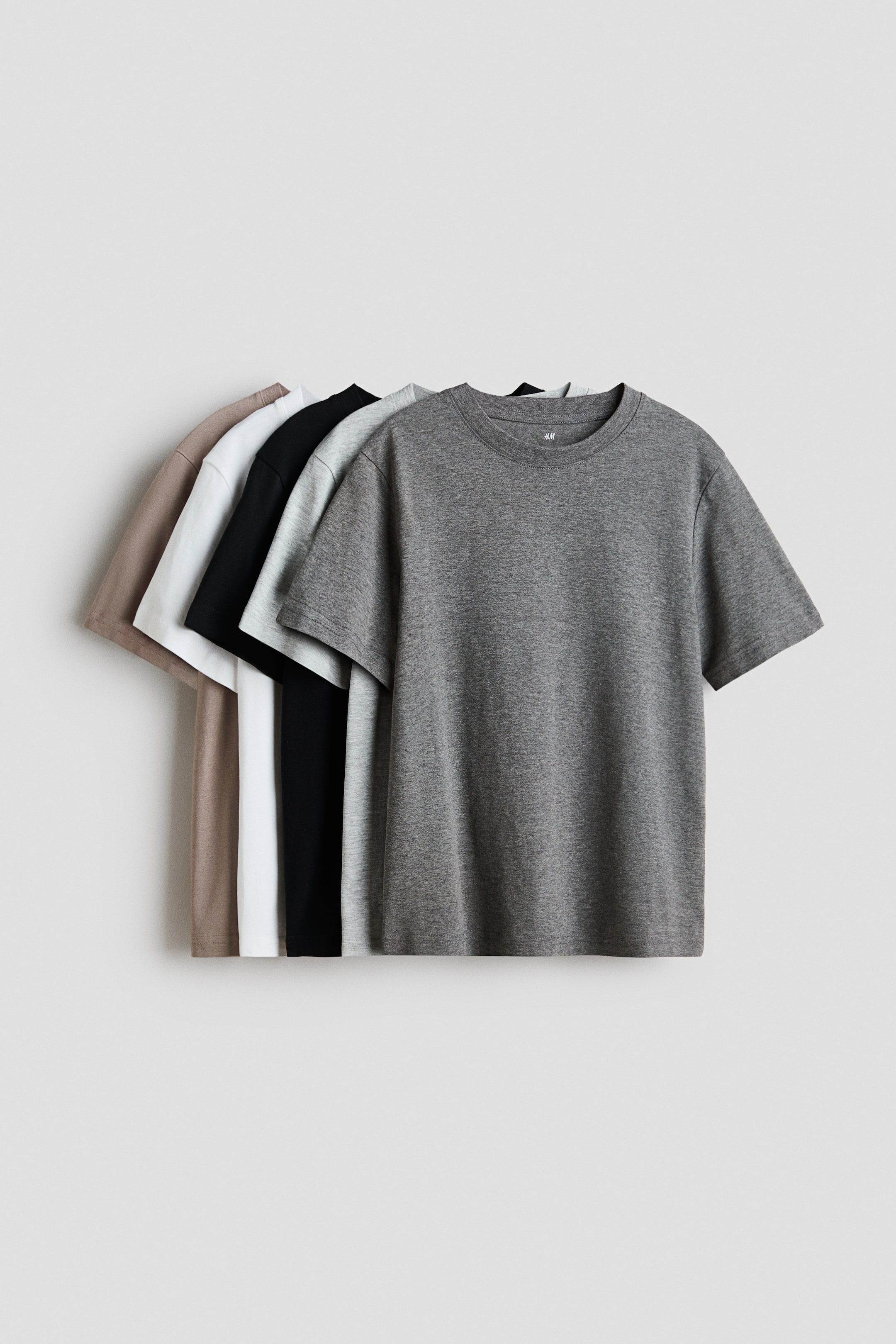Größeres Bild anzeigen: Fünf T-Shirts aus weichem Baumwoll-Jersey mit Rundhalsausschnitt und gerade geschnittenem Saum sind sichtbar geschichtet und zeigen ihre Vorderseite. Sie erscheinen in Dunkelgrau, Hellgrau, Schwarz, Weiß und Hellbraun.