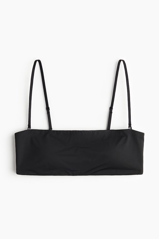 Un sujetador bandeau negro se presenta desde el FRENTE, con un tejido de jersey suave. Está diseñado como una banda recta, con dos tirantes delgados, ajustables y desmontables que se extienden hacia arriba desde el borde superior, y no se ven cierres. - 1