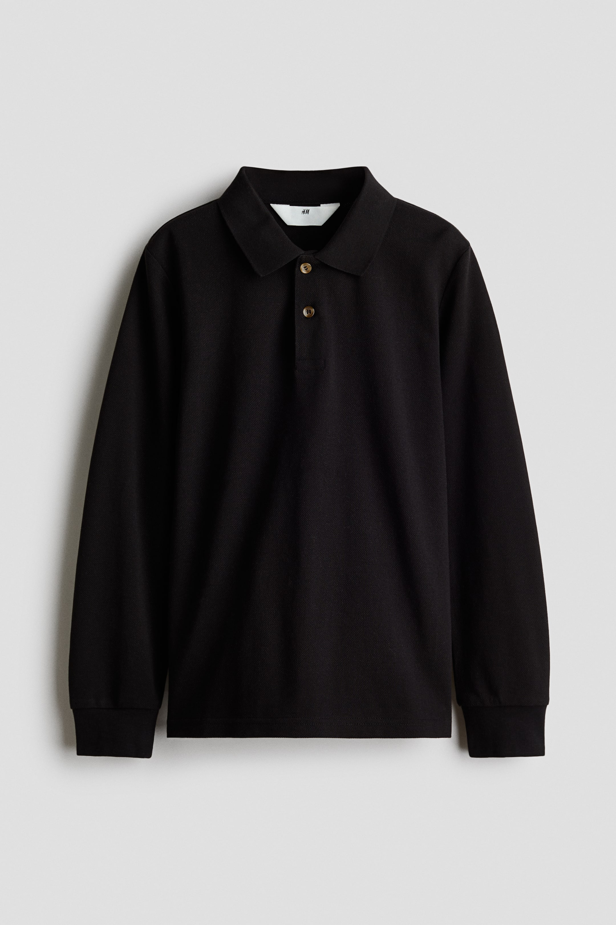 View larger image: The black long-sleeved polo shirt is showcased from the front, highlighting its textured knit fabric. It boasts a classic spread collar, a two-button placket adorned with light brown buttons, long sleeves with ribbed cuffs, and a white rectangular tag visible beneath the collar.