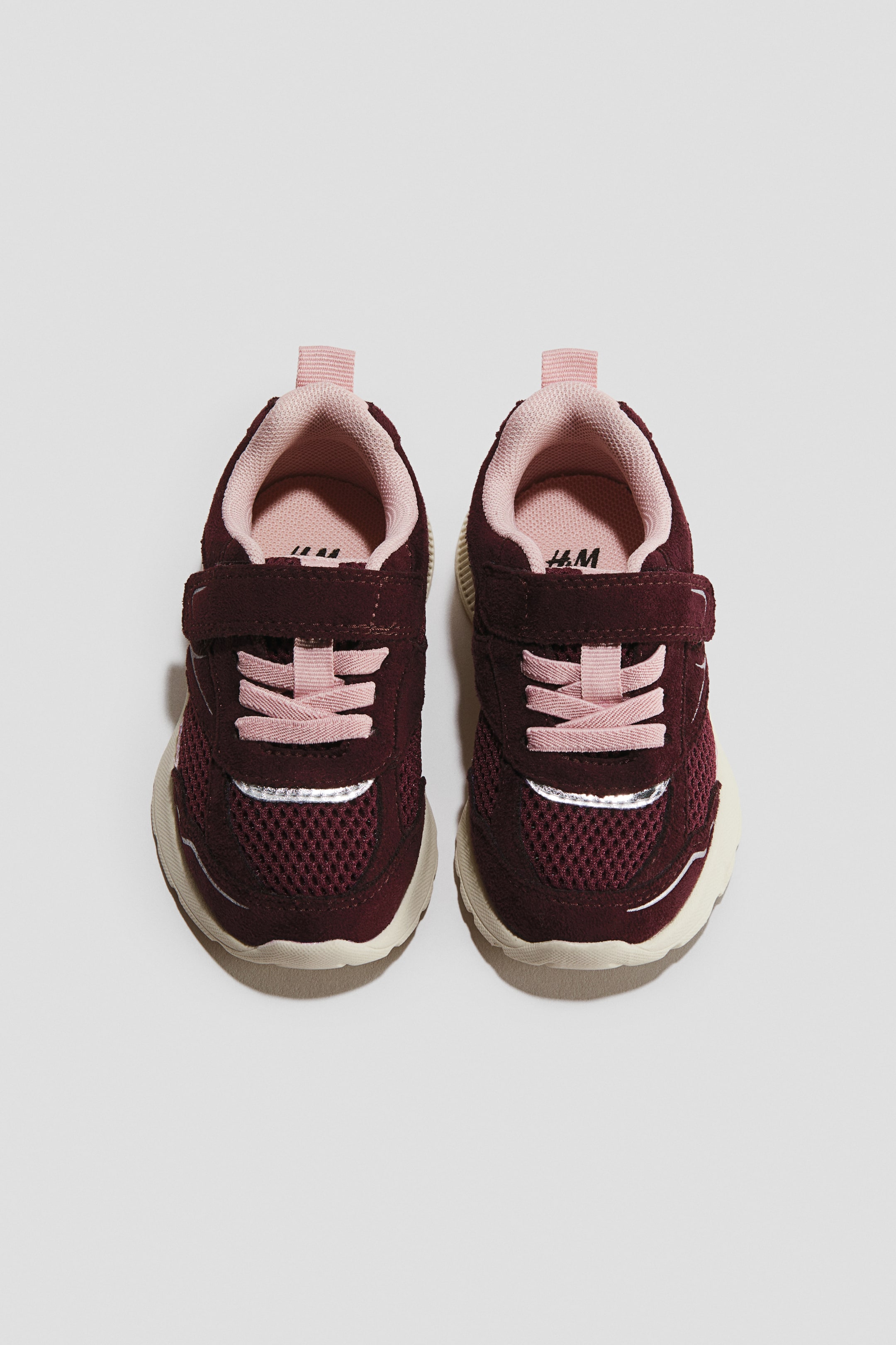 Προβολή μεγαλύτερης εικόνας: Ένα ζευγάρι sneakers φαίνεται από μπροστά, αναδεικνύοντας επάνω μέρος από μπορντό mesh και suede με ένα μονό λουράκι hook-and-loop πάνω από ανοιχτό ροζ ελαστικά κορδόνια. Ο σχεδιασμός περιλαμβάνει ανοιχτό ροζ εσωτερική επένδυση, πίσω θηλιά έλξης, ασημί αντανακλαστική ρίγα και ογκώδεις εξωτερικές σόλες σε χρώμα κρεμ.