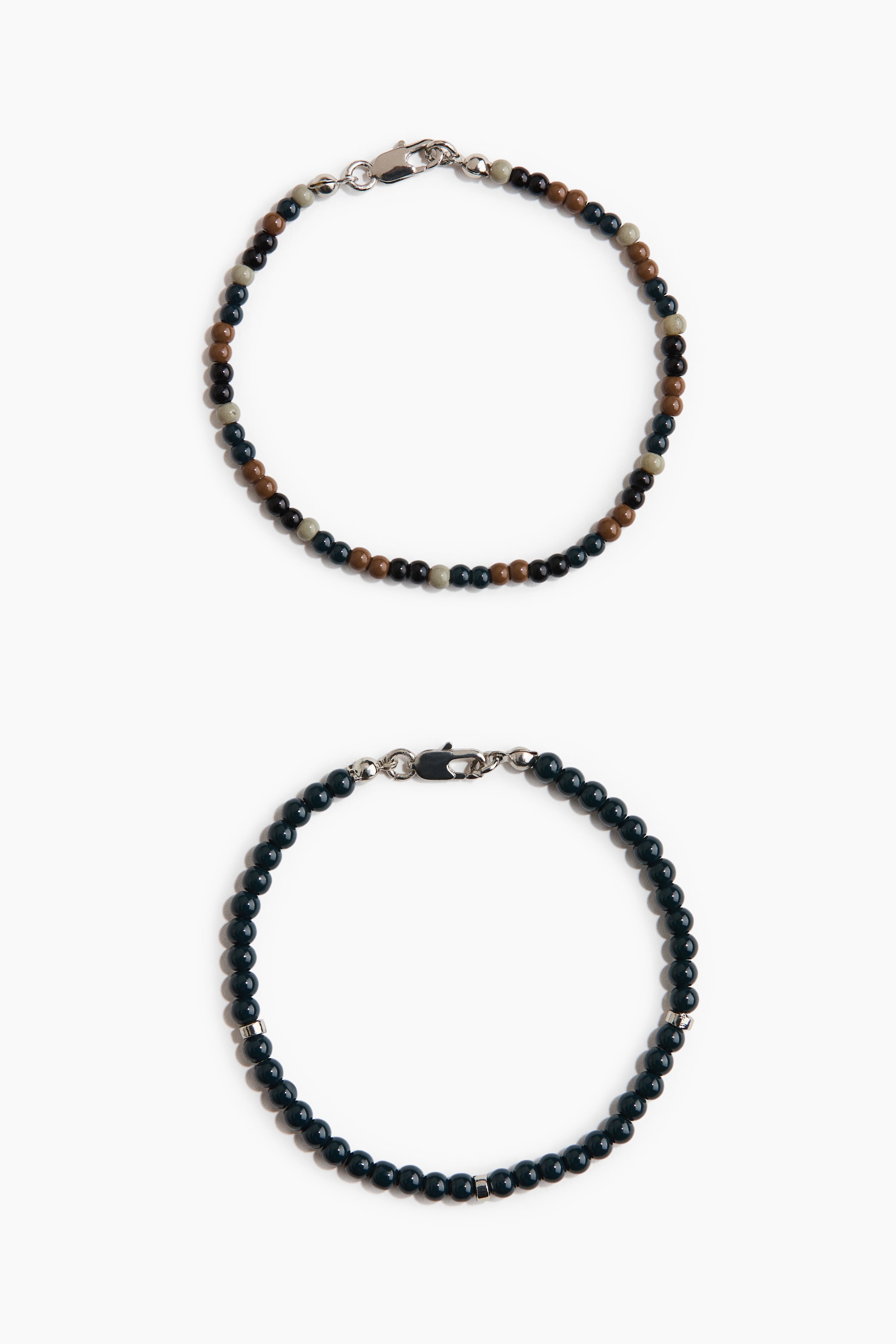 Ver imagen más grande: Dos pulseras con cuentas están dispuestas de manera plana en formas circulares, cada una con un cierre de langosta en tono plateado. La pulsera superior presenta pequeñas cuentas redondas en marrón, negro, verde azulado oscuro y gris claro; la pulsera inferior muestra pequeñas cuentas redondas de color azul oscuro intercaladas con dos cuentas cilíndricas en tono plateado.