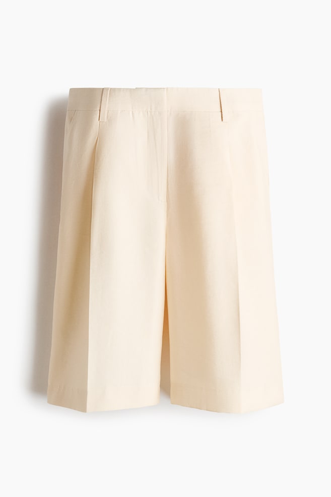 Cream wide-leg shorts are featuring a flat waistband with belt loops and a single front pleat on each leg, extending to a knee-length silhouette. - 1