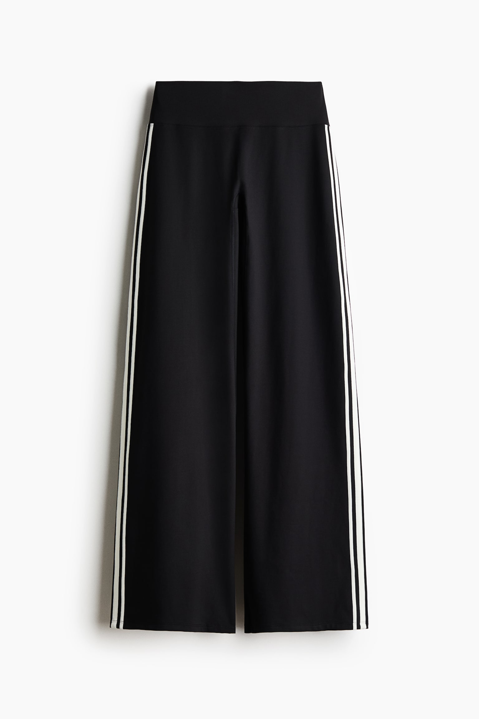 Black wide-leg trousers are shown from the front, featuring a high, flat waistband and a relaxed silhouette. Two thin vertical white stripes run down the outer side of each leg.