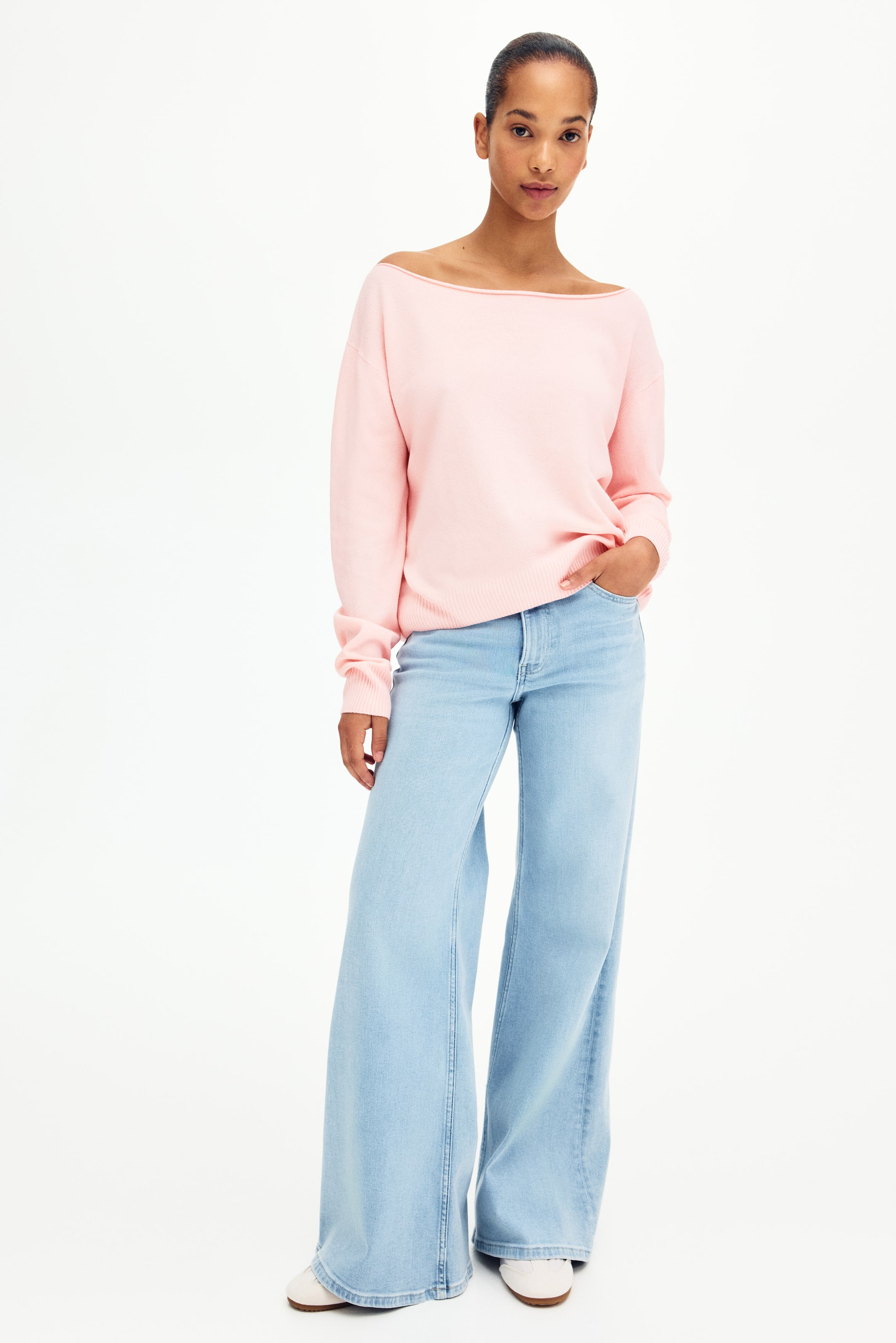 查看大圖: 淺粉紅色毛衣展示了船領設計，肩膀略微下垂，並配有羅紋袖口和下擺。淺藍色寬腿牛仔褲呈現出輕鬆流暢的版型，並設有前口袋。
