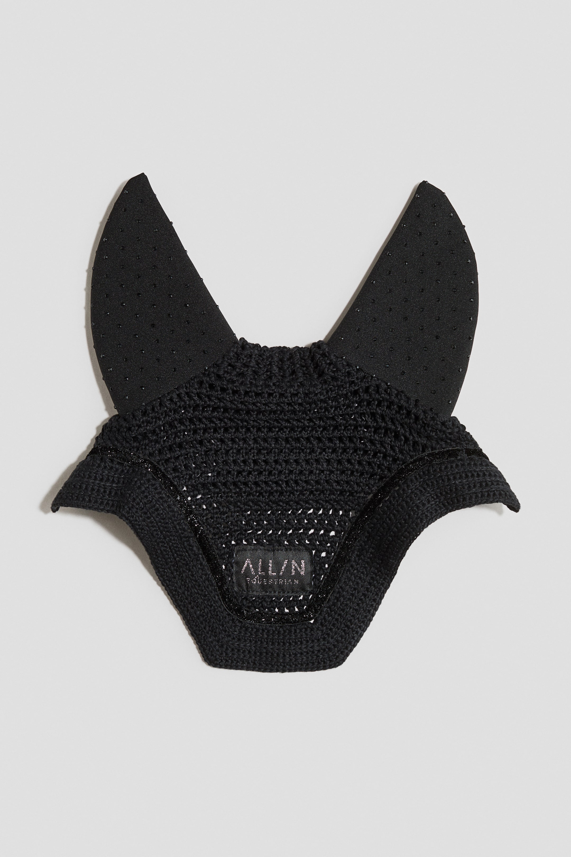 Größeres Bild anzeigen: Ein schwarzes Reitohrenhaube ist nach VORNE gerichtet und verfügt über einen gehäkelten Mesh-Hauptteil sowie feste Stoffohren, die mit kleinen, gleichmäßig verteilten Punkten verziert sind. Ein subtiler Glitzerbesatz verläuft entlang des Mesh-Randes, ein festes Strickband bildet den unteren Abschluss, und ein 'ALL/N EQUESTRIAN'-Label ist auf der Vorderseite sichtbar.