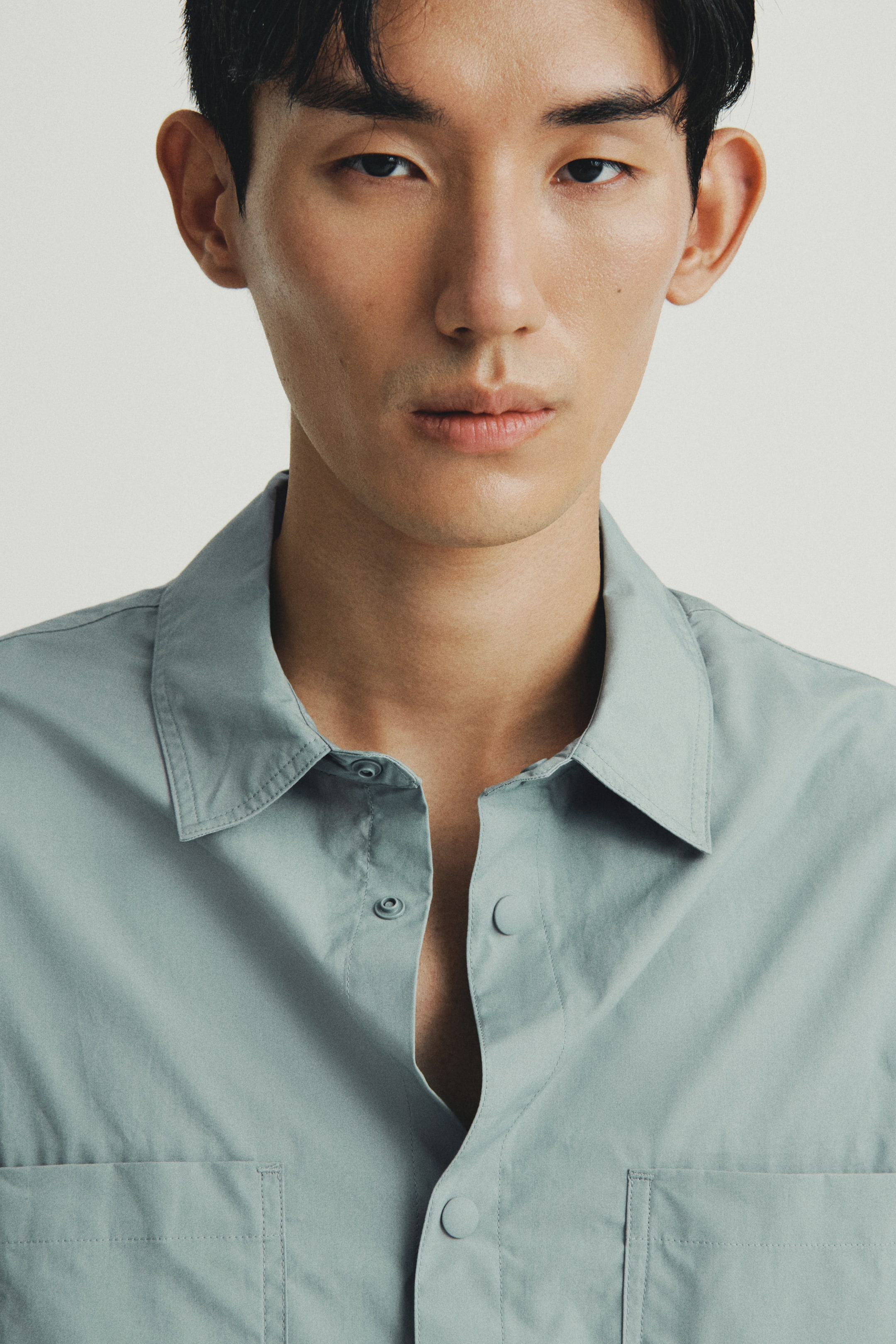 View larger image: A pale teal shirt is being presented from the front, showing its upper portion, featuring a classic pointed collar and two patch pockets on the chest. The front placket is displaying matching round buttons, with the top two buttons currently unfastened.