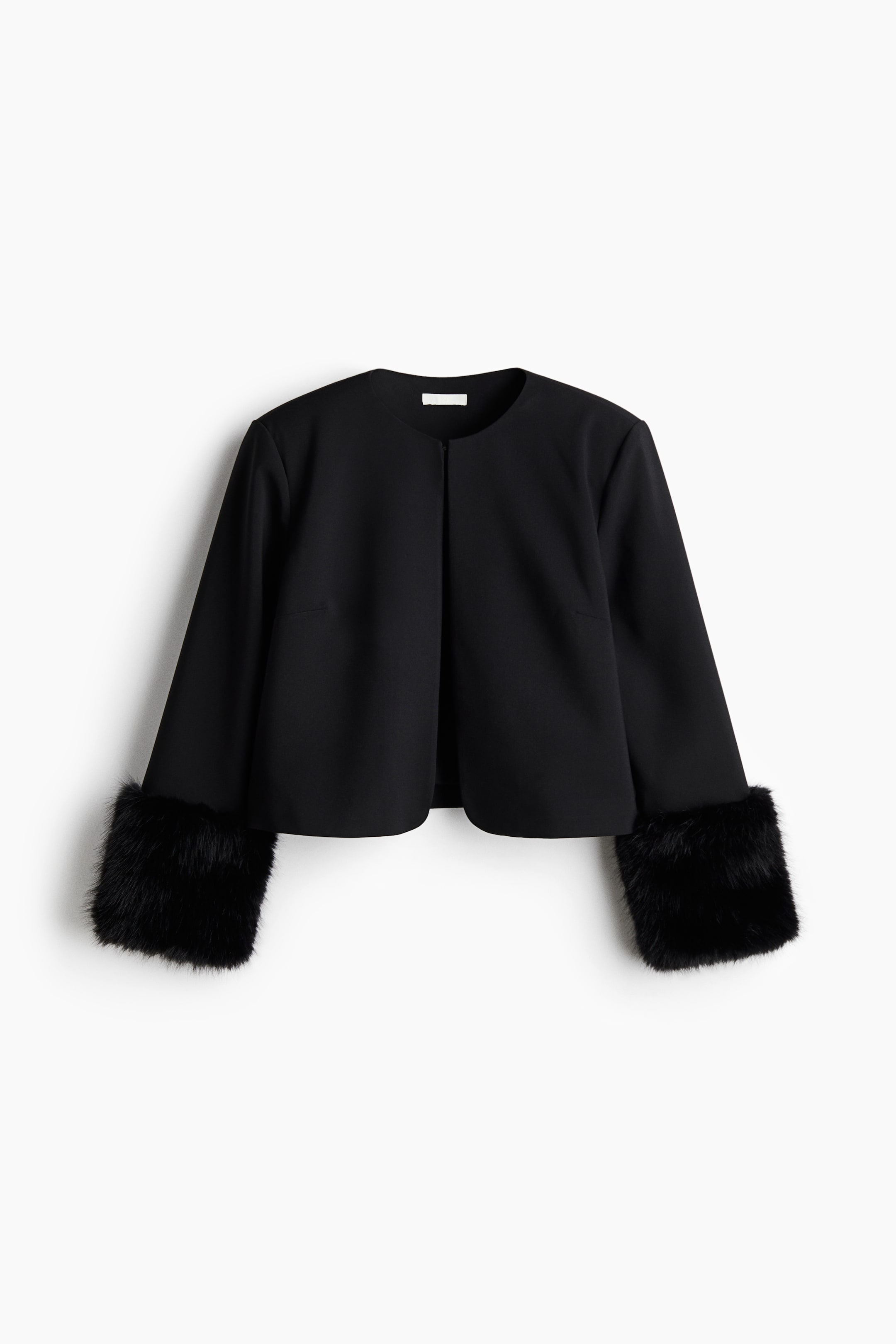 View larger image: A black cropped jacket features a collarless, round neckline and long sleeves, and is finished with wide black faux fur cuffs.