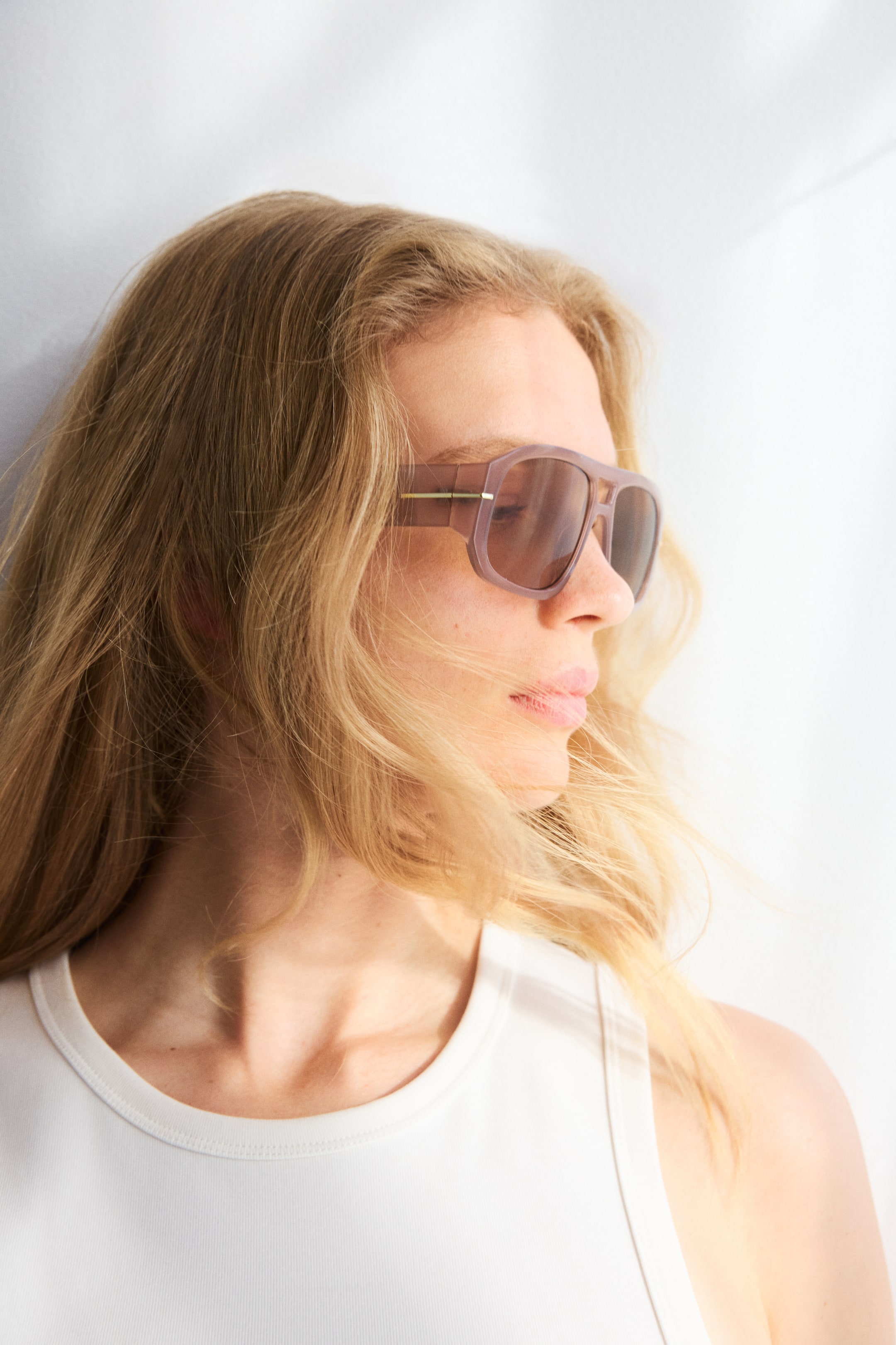 View larger image: These sunglasses showcase robust, translucent light brown square frames paired with dark-tinted lenses. The design is enhanced by a slender gold-toned metal detail on the temples, elegantly worn and oriented towards the right.