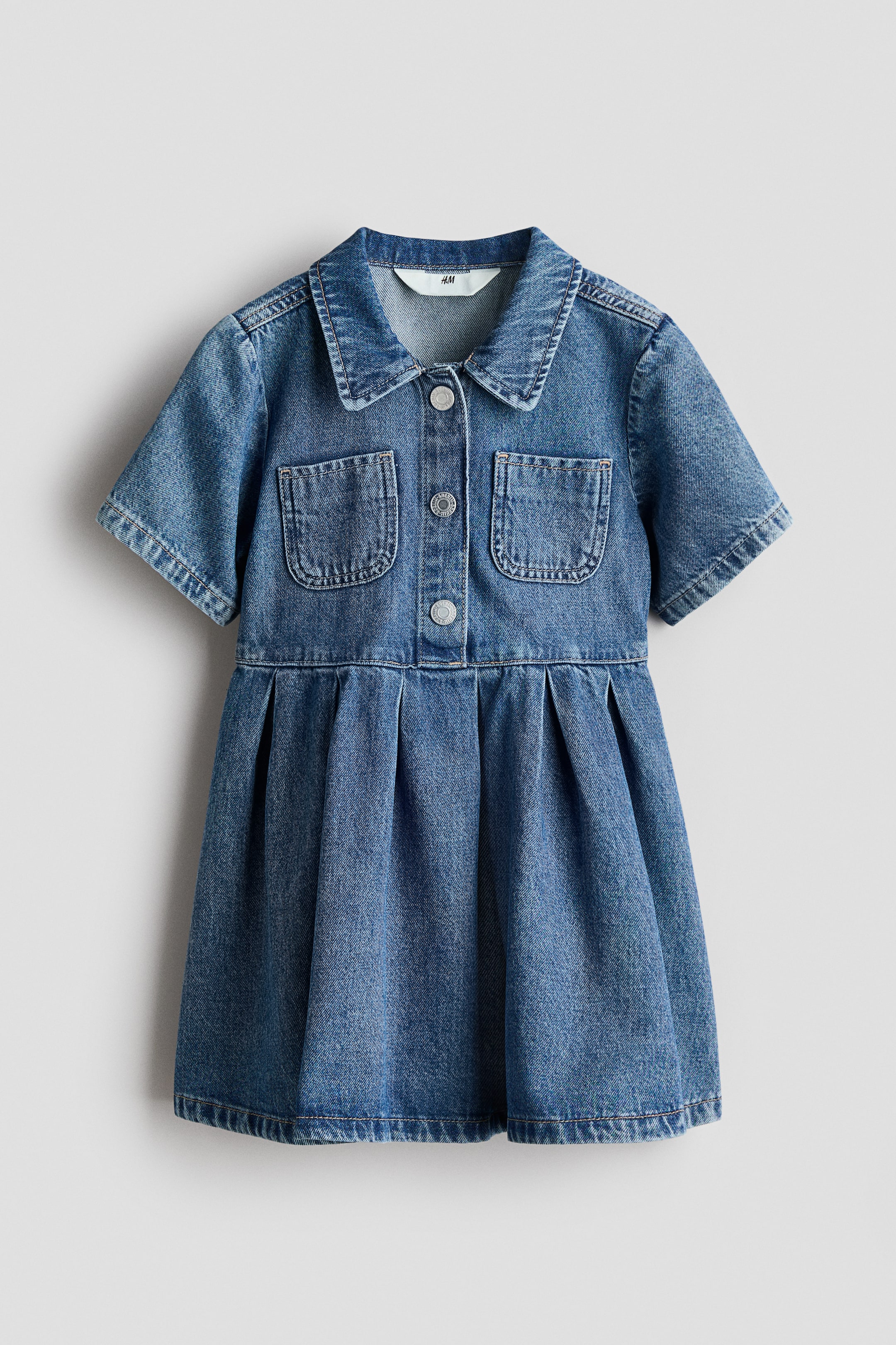 Voir une image plus grande: Une robe en denim bleu est présentée de face, avec un col pointu, des manches courtes et une patte de boutonnage pleine longueur avec des boutons argentés. Deux poches poitrine avec rabats sont visibles, et la jupe est froncée à la taille.