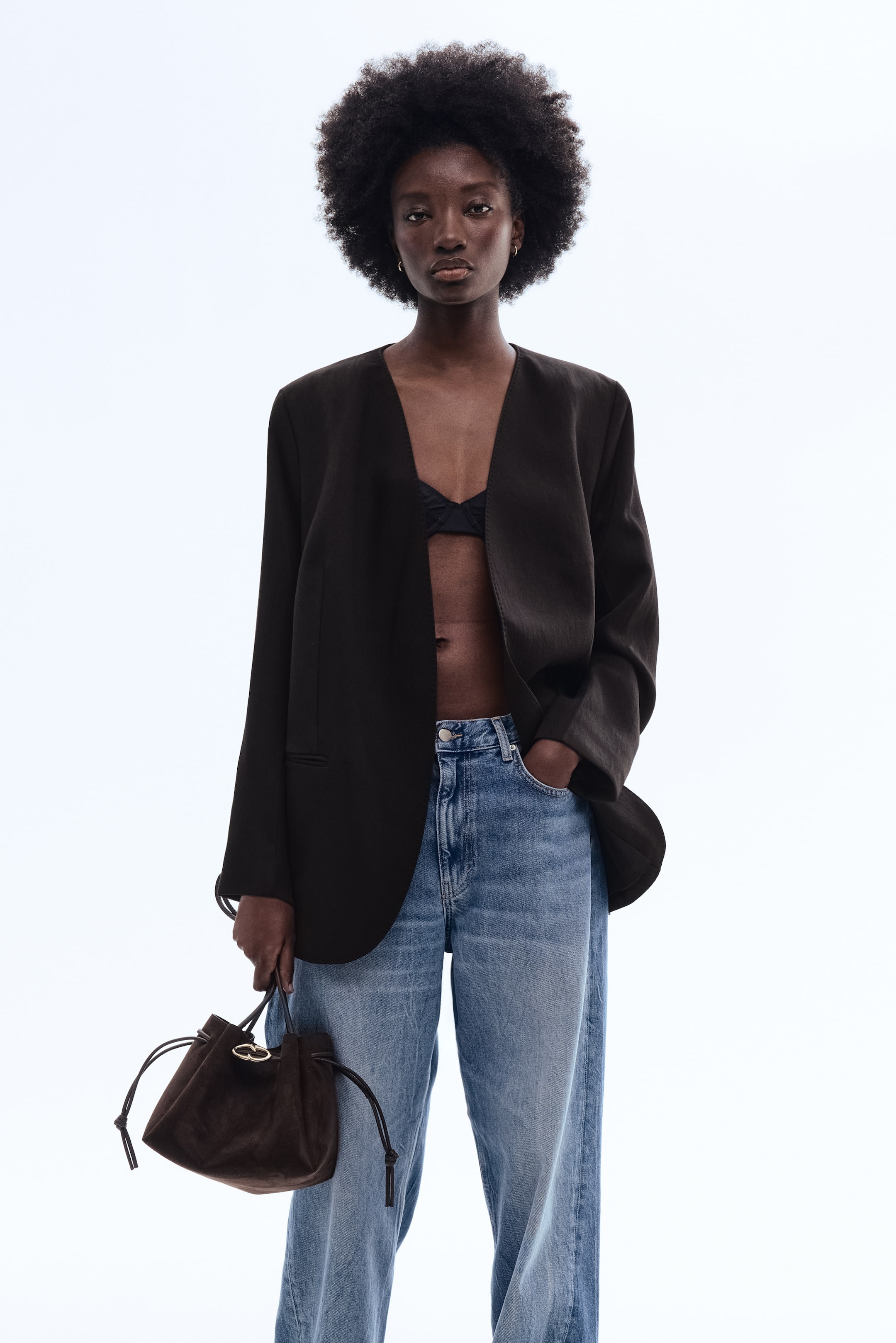 View larger image: A dark brown blazer is facing front, featuring a collarless design with a deep V-neck opening. It is presenting a relaxed, slightly oversized fit with long sleeves and a subtle welt pocket detail on the left side, styled open.