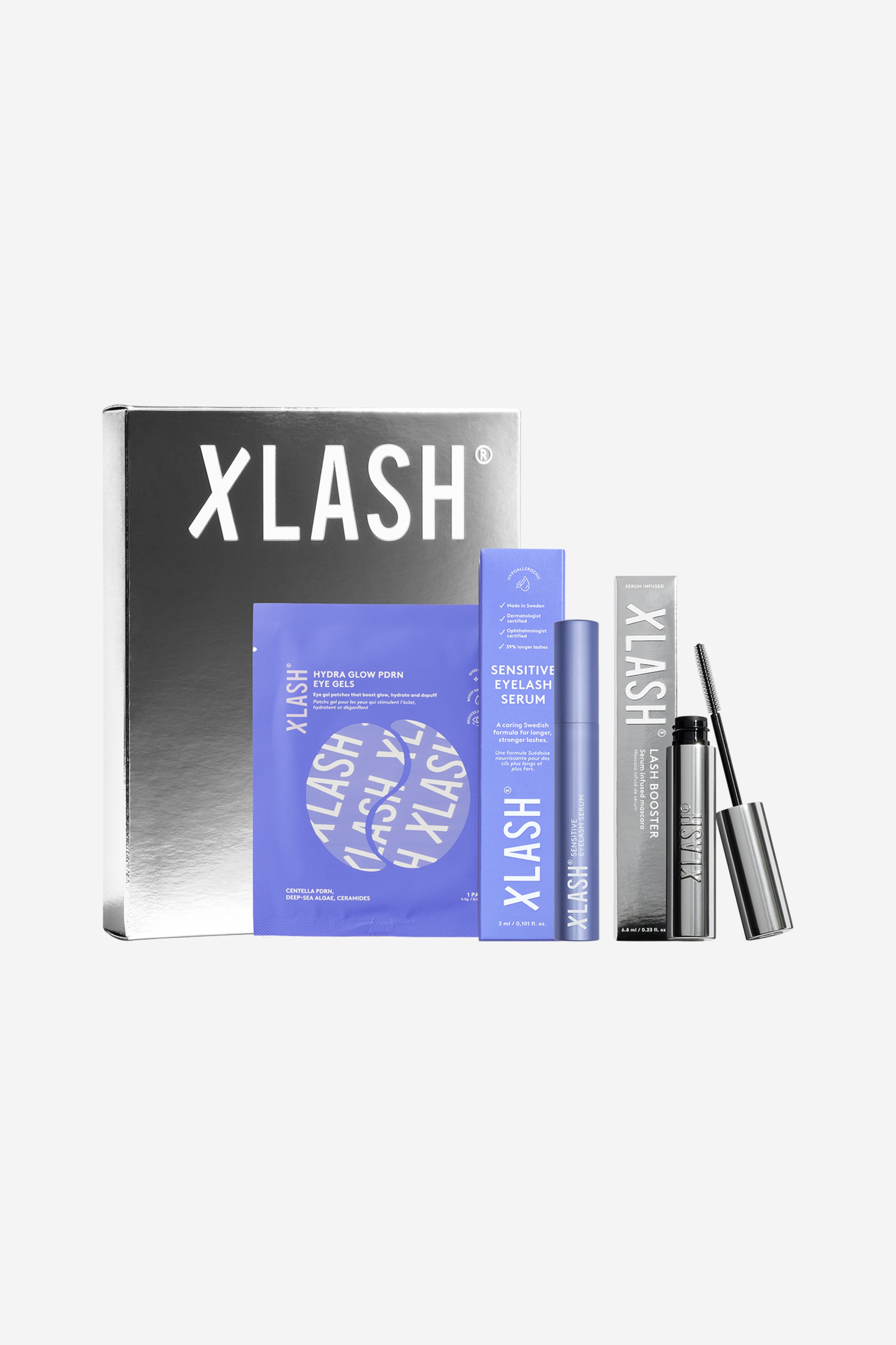 Visa större bild: Ett XLASH-skönhetsgåvoset visar en stor, reflekterande silverfärgad ask som står bakom en blåviolett ögongel-sachet, en periwinkleblå box med lash serum och dess tillhörande tub, samt en silverfärgad lash booster-box med sin tub och den utdragna applikatorborsten som vilar till höger.