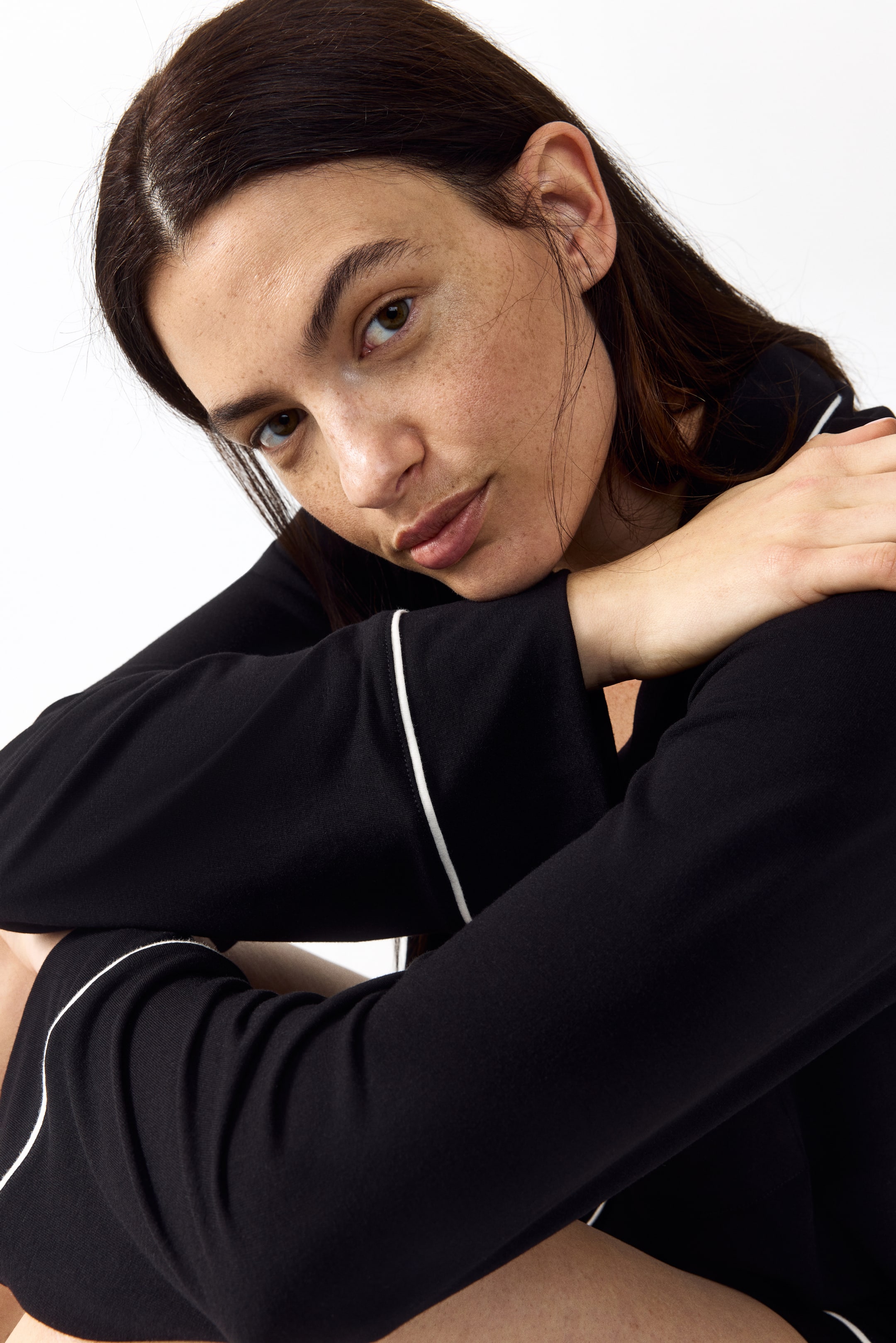 View larger image: The black long-sleeve top features white piping. The piping outlines the sleeve hems and a design line along the sleeves, crossing over and angled toward the viewer.