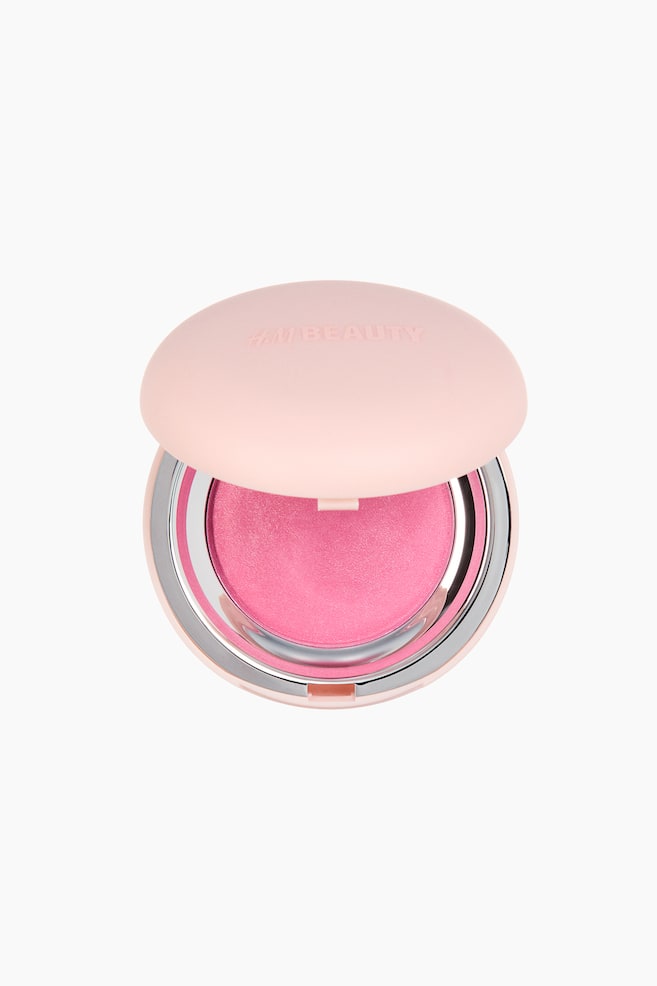 A cream-to-powder blusher compact is facing front, its light-pink lid open to reveal "H&M BEAUTY" embossed on top. The open compact reveals a circular pan of vibrant pink blusher, encased by a shiny silver metallic rim. - 1