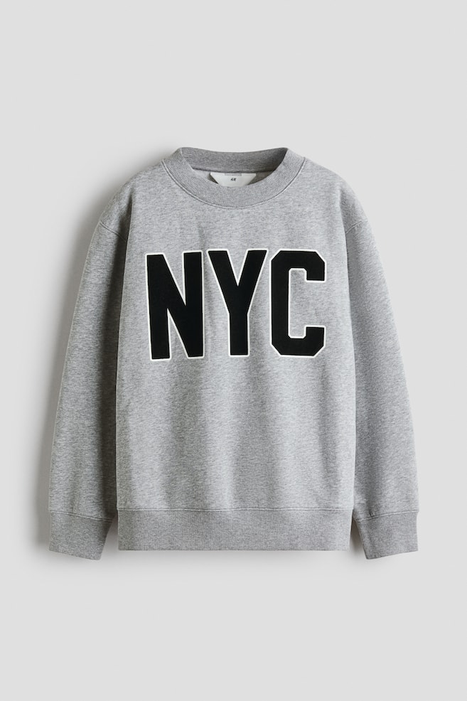A grey sweatshirt is displaying its front, featuring "NYC" in large black letters with a white outline across the chest. It is designed with a ribbed crew neck, ribbed cuffs, and a ribbed hem. - 1