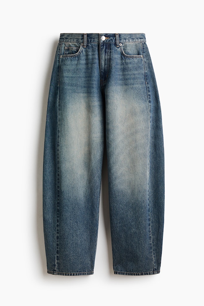 A pair of medium-wash blue denim jeans is shown from the front, featuring a regular waist with belt loops, a zip fly with a button, and a classic five-pocket design. The jeans showcase a curved, voluminous leg silhouette that tapers towards the hems, highlighted by faded detailing down the centre of each leg. - 1