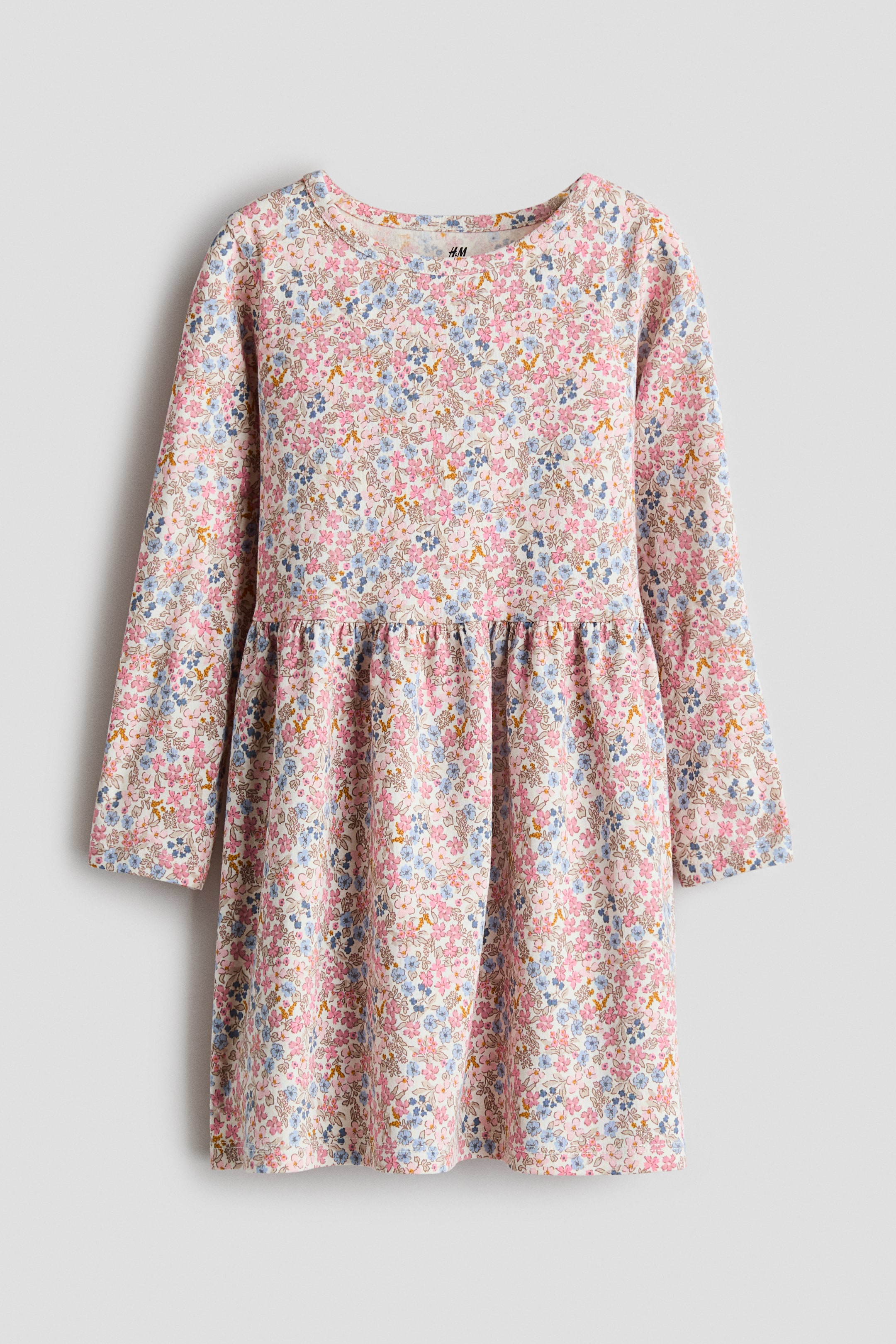 View larger image: A children's dress showcasing a delicate floral pattern in pink, blue, and yellow on a light backdrop. It features long sleeves, a round neckline, and a gathered waist seam that creates a flared skirt.