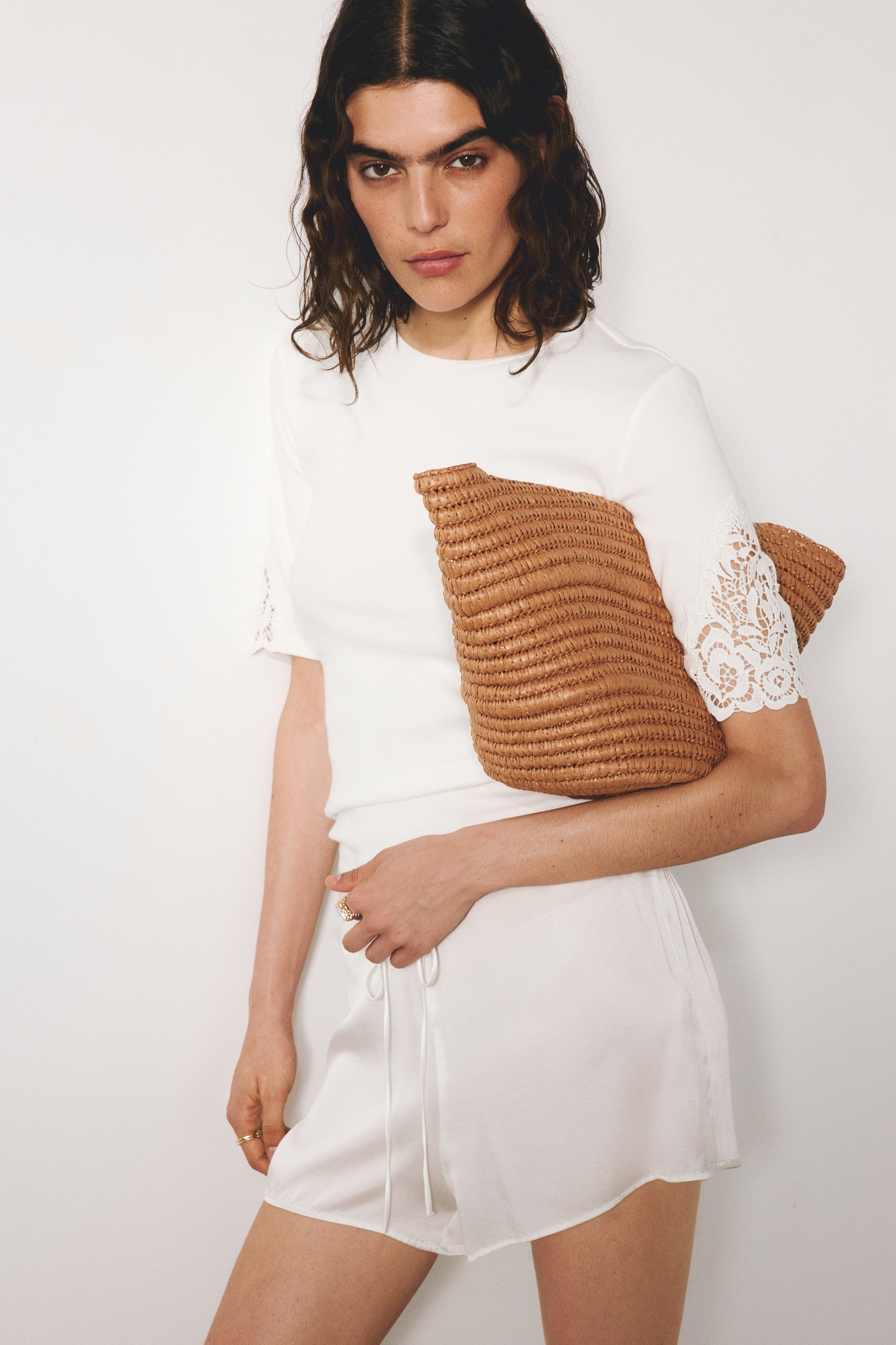 View larger image: The model is wearing a fitted top made from ribbed cotton jersey, featuring a round neckline and short sleeves with lace insets. She is holding a woven clutch bag by her side.