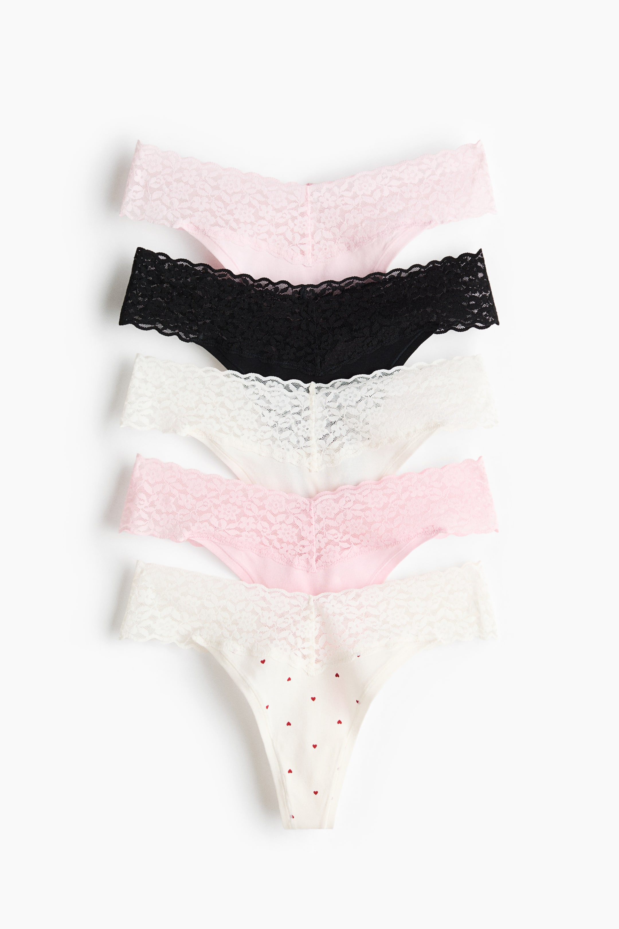 Visualizza immagine più grande: Cinque slip a perizoma, presentati frontalmente, sono impilati, mostrando vari colori e motivi. Ogni slip presenta una cintura in pizzo a forma di V bassa e lati stretti. La collezione include slip in rosa chiaro, nero, bianco e un bianco sporco con piccoli motivi a cuore rosso.
