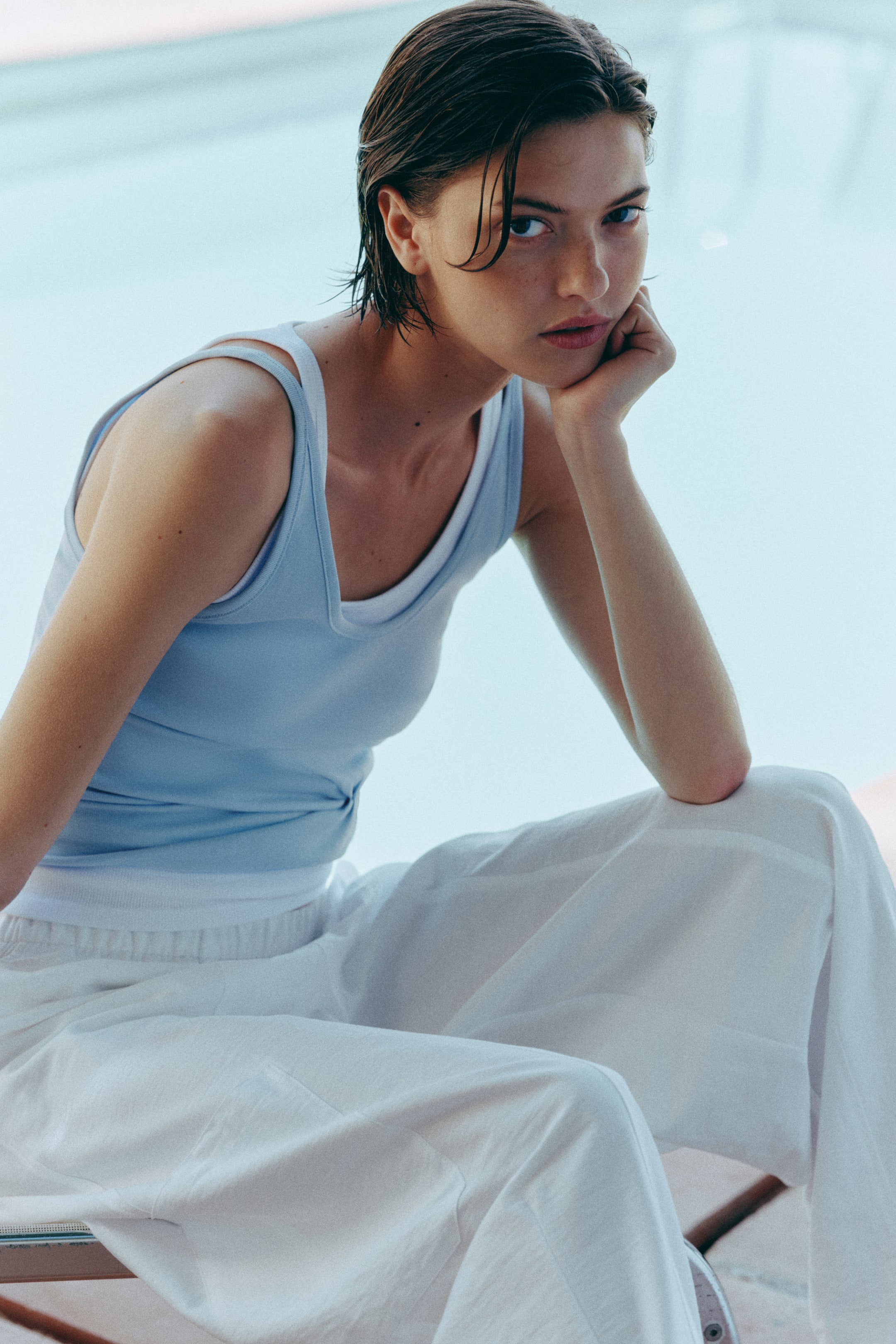 View larger image: A light blue ribbed tank top is worn over a white tank top, both featuring scoop necks and thin straps, with the light blue top appearing form-fitting. White wide-leg pants with an elasticated waistband are also worn, presenting a loose and flowing fit.