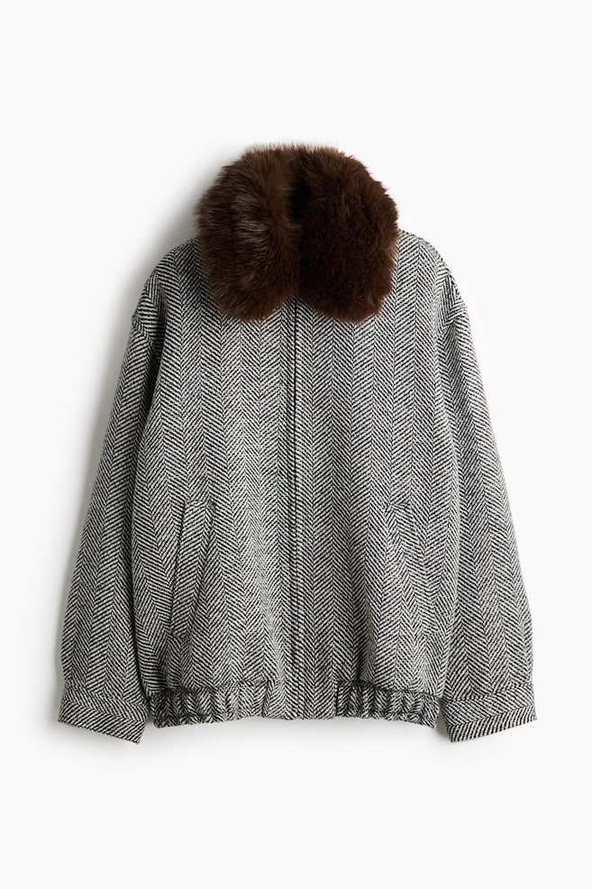 Una chaqueta de espiga en blanco y negro muestra un cuello afelpado de pelo sintético marrón en esta vista frontal. La chaqueta presenta un cierre delantero con cremallera oculta, bolsillos de ojal inclinados y un bajo elástico. - 1