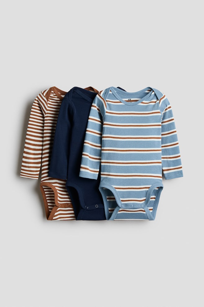 Three long-sleeved baby bodysuits are overlapping in a front-facing view, showcasing envelope necks and press-stud fastenings at the bottom. The set includes one bodysuit in white with brown horizontal stripes, one in solid navy blue, and one in light blue with white and brown horizontal stripes. - 1