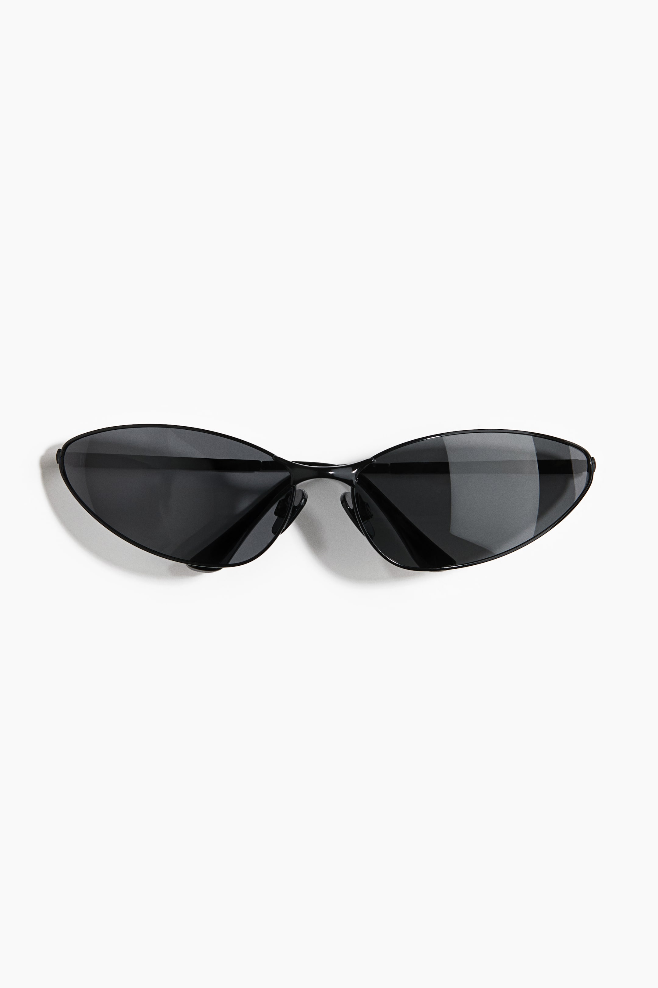 View larger image: Sunglasses featuring narrow black plastic frames and dark tinted lenses are resting front-facing, displaying a sleek, aerodynamic silhouette with elongated, almond-shaped lenses.