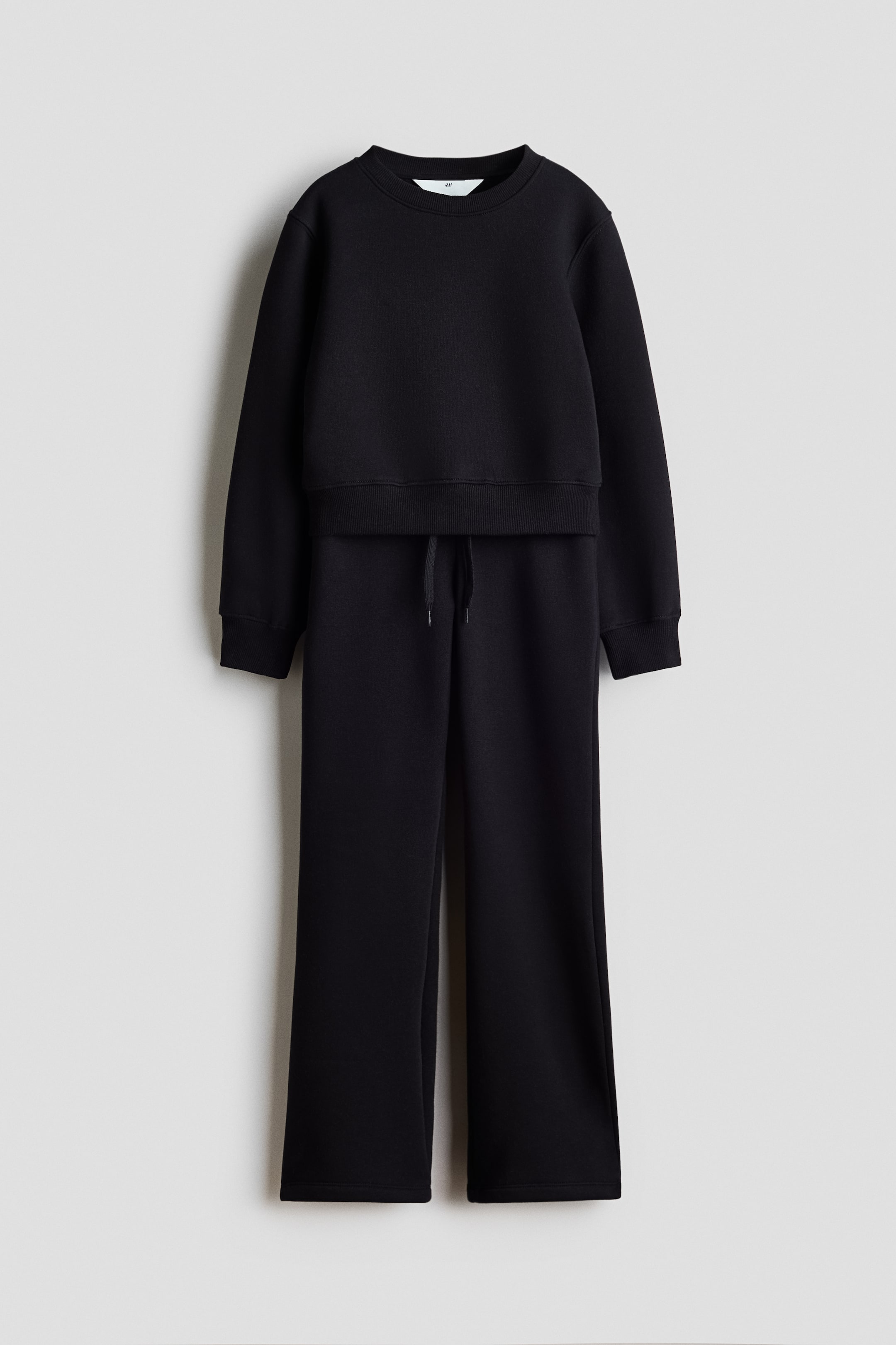 Agrandir l'image: Un ensemble de détente noir en deux pièces est présenté de face, comprenant un sweat-shirt à col rond avec des poignets et un ourlet côtelés, ainsi qu'un pantalon à jambes larges avec une taille à cordon de serrage visible.