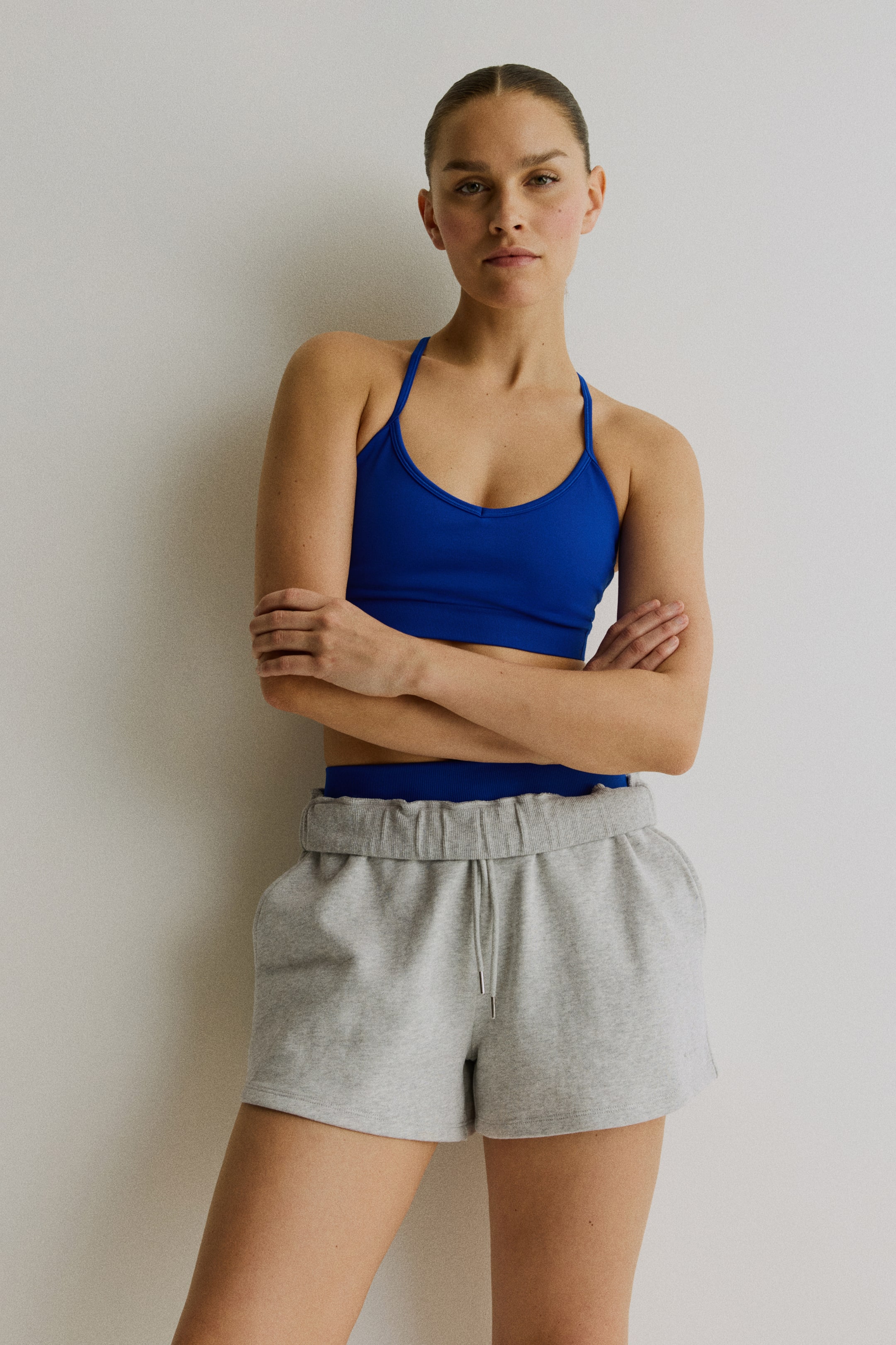 View larger image: The model is wearing grey regular-fit sweatshorts, which feature covered elastic and a drawstring at the waist, along with diagonal side pockets. The sweatshorts are styled with a blue crop top.