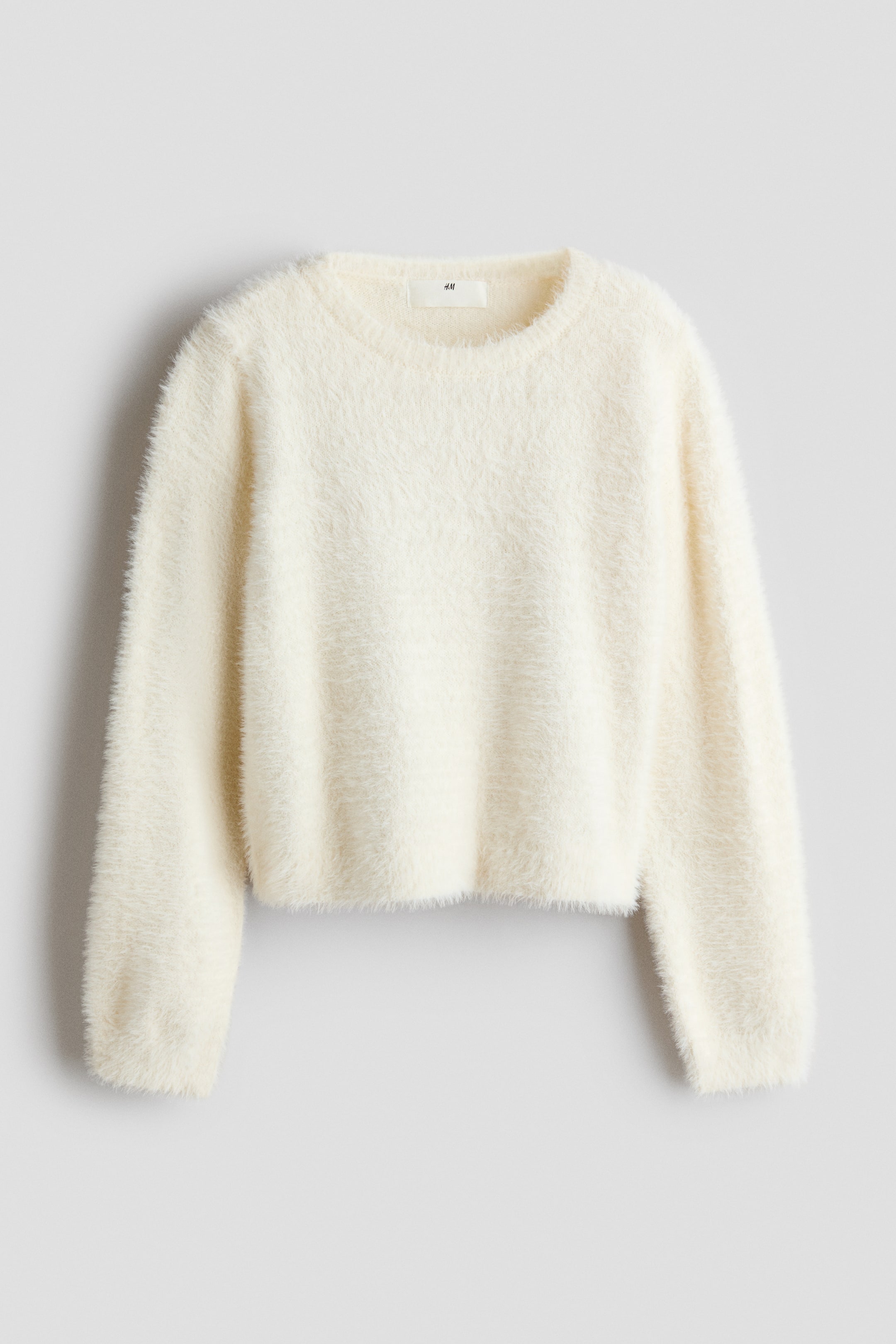View larger image: A cream-coloured, fluffy knit sweater is shown from the front, featuring a round crew neck, long sleeves, and a soft, eyelash-textured finish. The sweater has a slightly cropped, straight-cut hem.