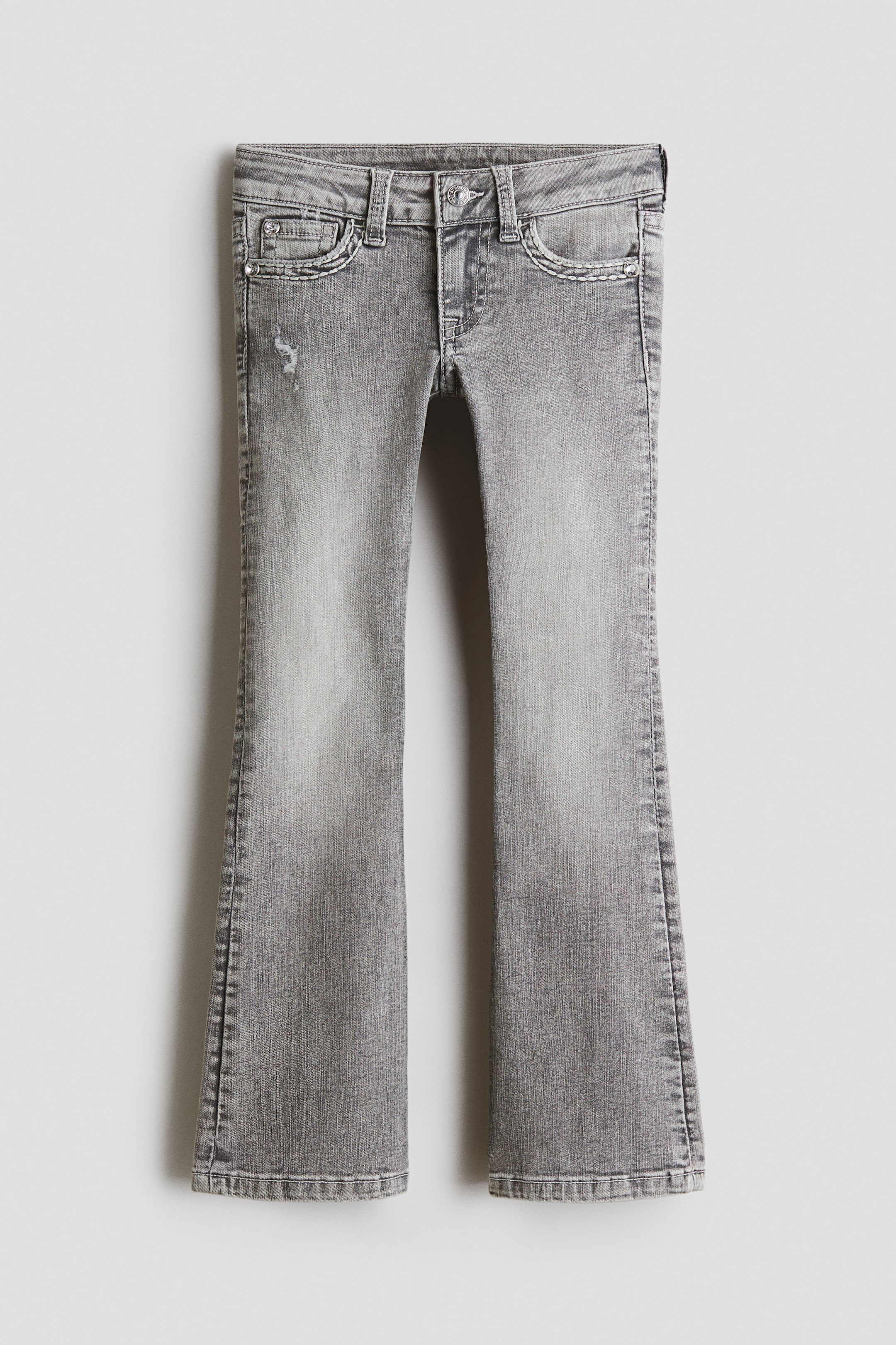 Agrandir l'image: Le jean en denim délavé gris présente une silhouette bootcut, ajustée de la taille à la cuisse puis s’évasant du genou jusqu’à l’ourlet. Ce jean taille basse est doté d’une braguette zippée avec fermeture par bouton, de poches avant, d’une poche ticket et de détails usés sur le haut de la jambe gauche.