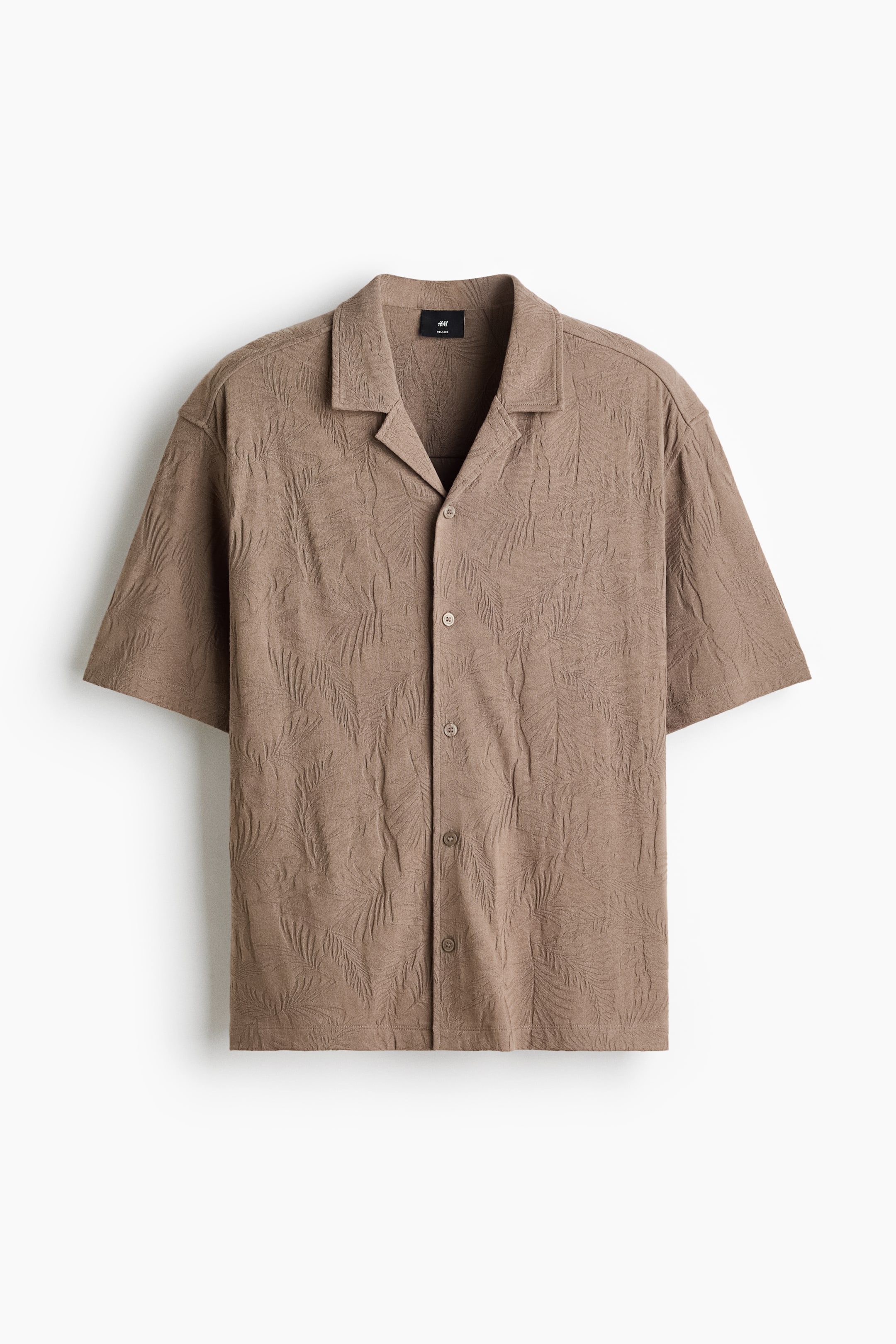 Ver imagen más grande: Una camisa marrón de manga corta, vista de frente, muestra un estampado en relieve de hojas de palma. Presenta un cuello de solapa y cierre frontal con botones marrones a juego, ofreciendo un ajuste relajado.