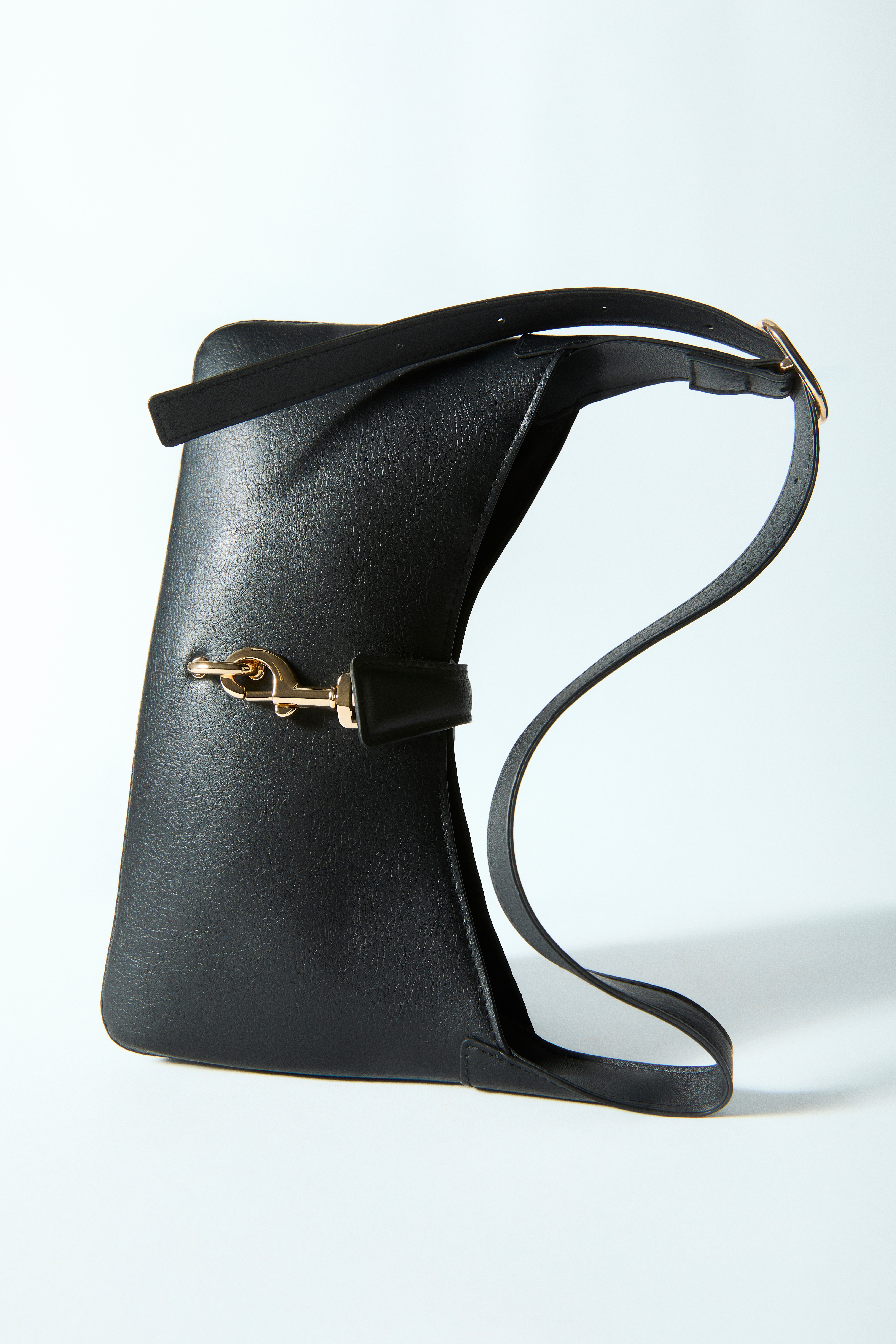 Eine schwarze Schultertasche mit strukturierter Oberfläche zeigt ihre Vorderseite, die durch eine geschwungene Silhouette und einen einzelnen Riemen besticht. Sie wird durch einen markanten goldfarbenen Karabinerverschluss in der Mitte gesichert.