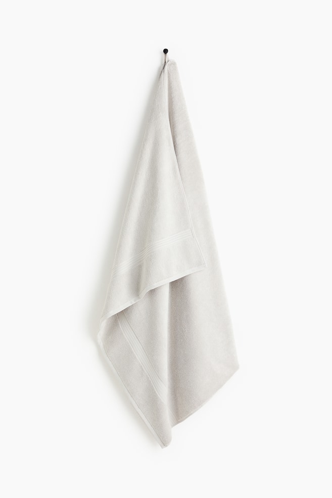 Une serviette gris clair est suspendue à un crochet, avec de subtiles bandes horizontales rayées près de ses bords. - 1