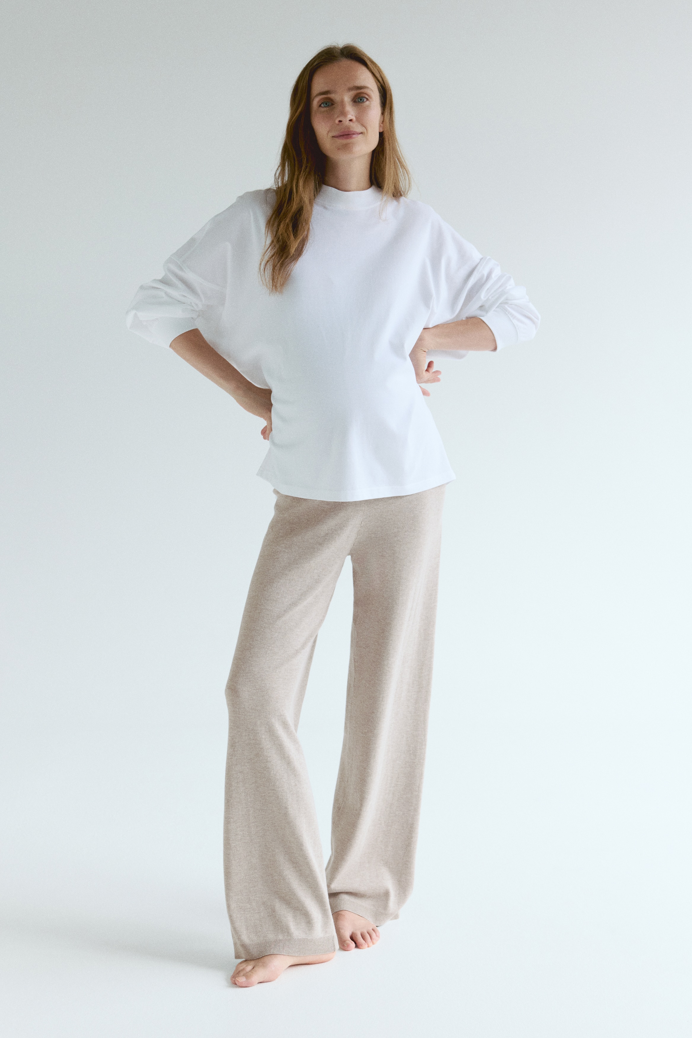 Beige Strickhosen werden von hinten präsentiert und zeigen eine hohe, gerippte Taille sowie lange, weite Beine mit Rippungen an den Säumen.
