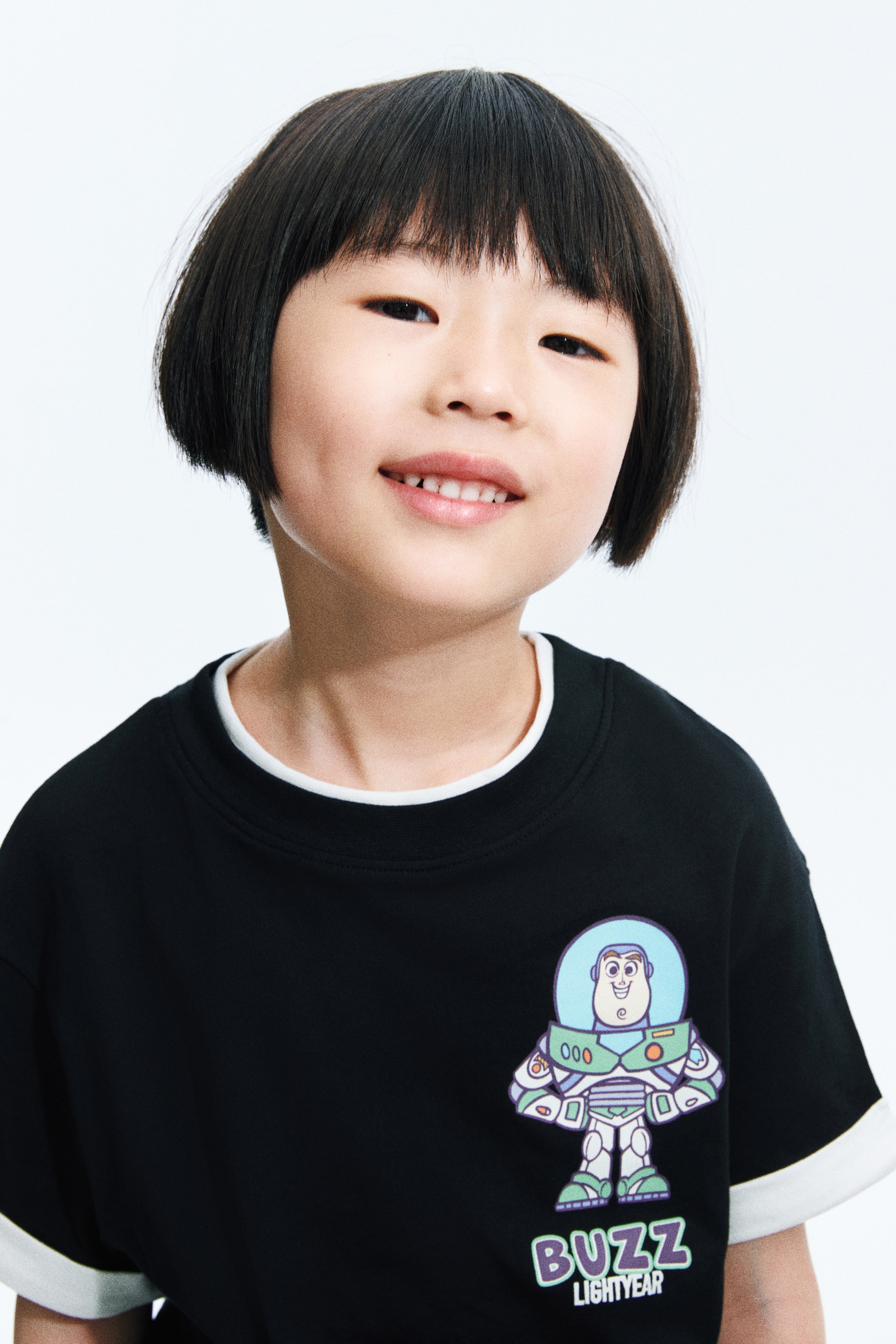 View larger image: The black short-sleeved top showcases a vibrant Buzz Lightyear graphic print on its front, with "BUZZ LIGHTYEAR" text beneath. A white long-sleeved top is layered underneath, visible at the crew neck and sleeve hems.