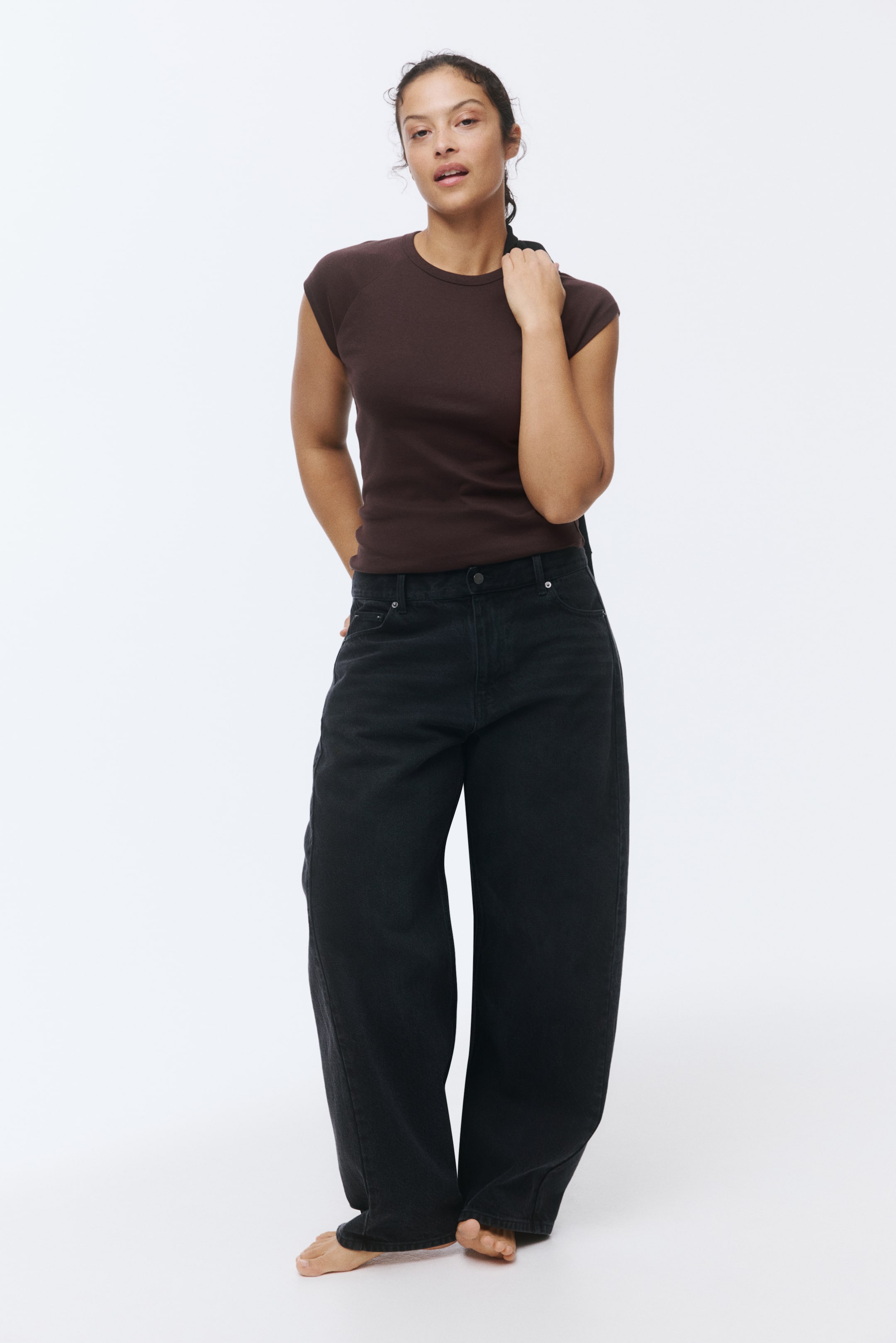 View larger image: A dark brown cap-sleeve crew neck top is being worn, tucked into black high-waisted wide-leg jeans that are pooling at the ankles.