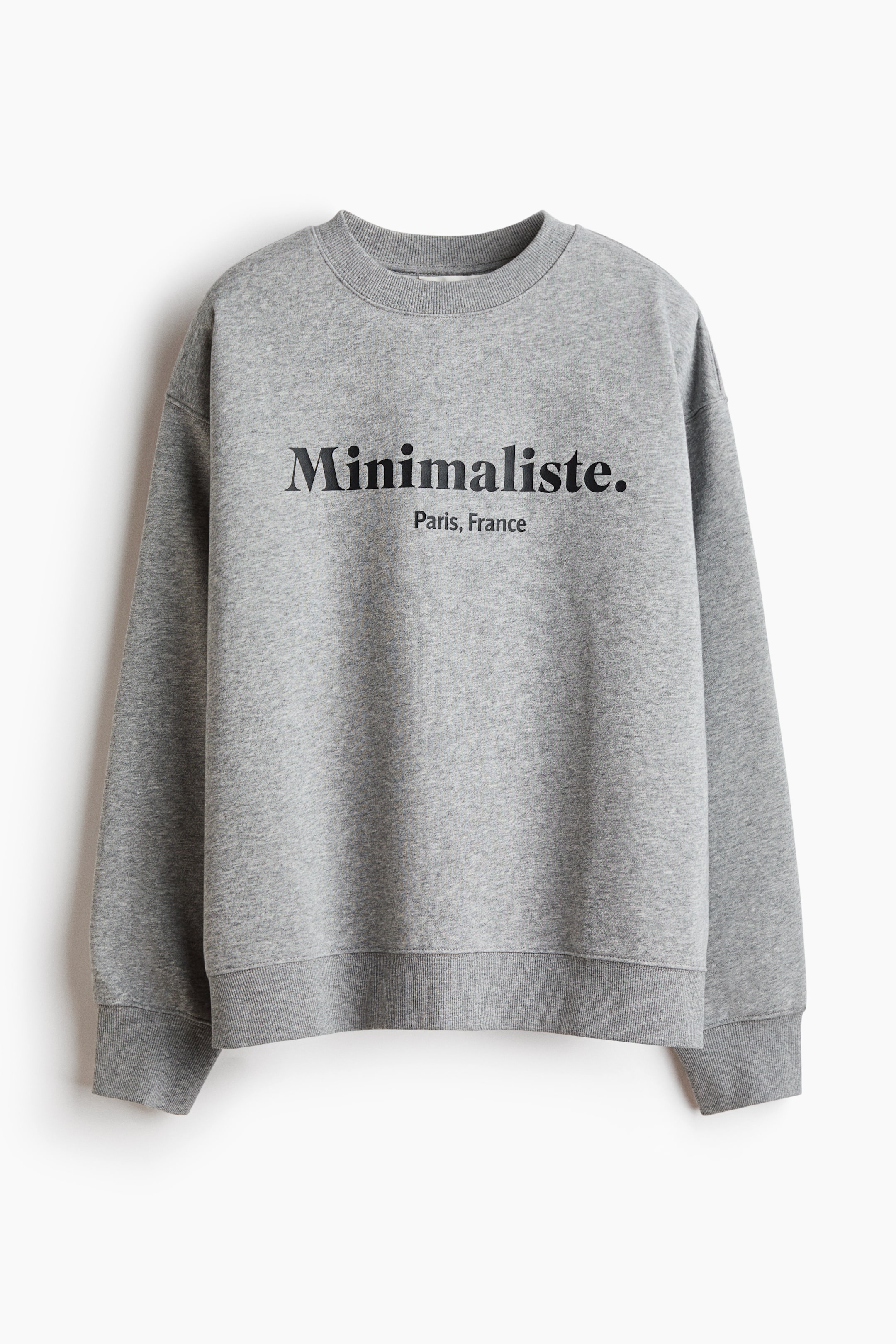 View larger image: An oversized, grey heathered sweatshirt is hanging front-facing, featuring a round rib-trimmed neckline, dropped shoulders, and long sleeves with ribbed cuffs and hem. The chest features the black printed text "Minimaliste." with "Paris, France" written underneath.